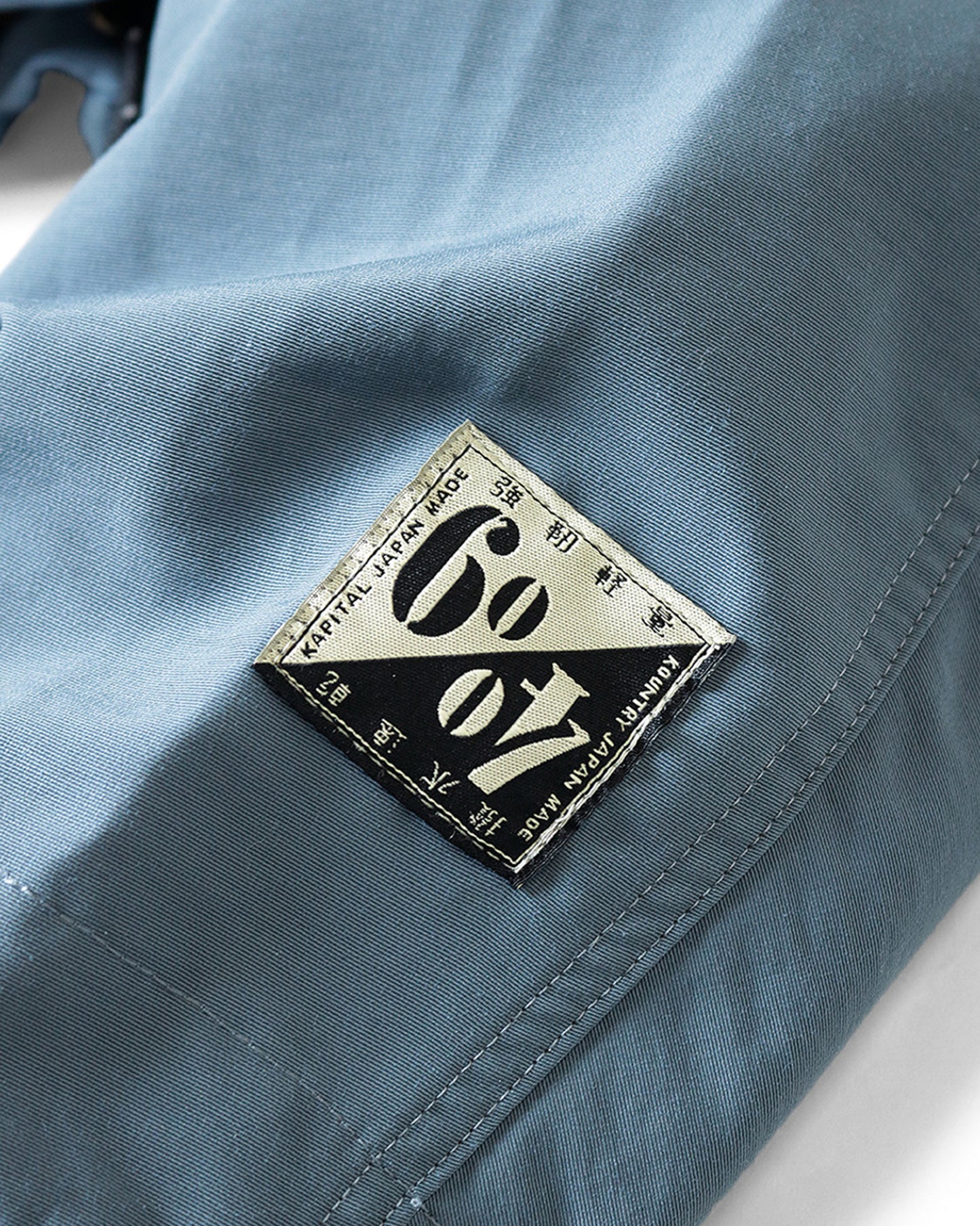 Cropped hooded rain jacket with two pockets in front. View of the logo patch.