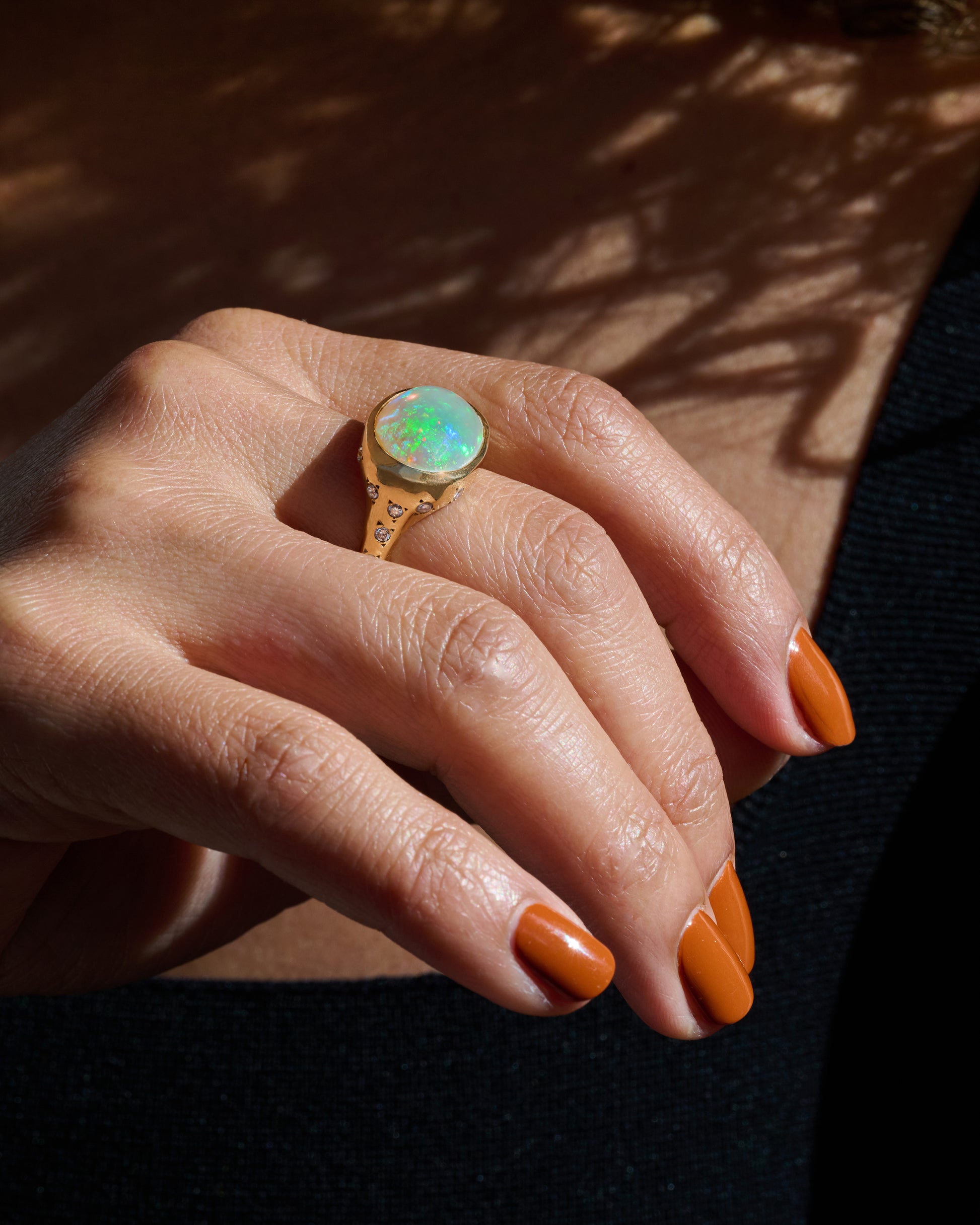 A polished yellow gold ring with a large east west oval Australian opal and diamonds on the setting and shoulders. View on a hand.