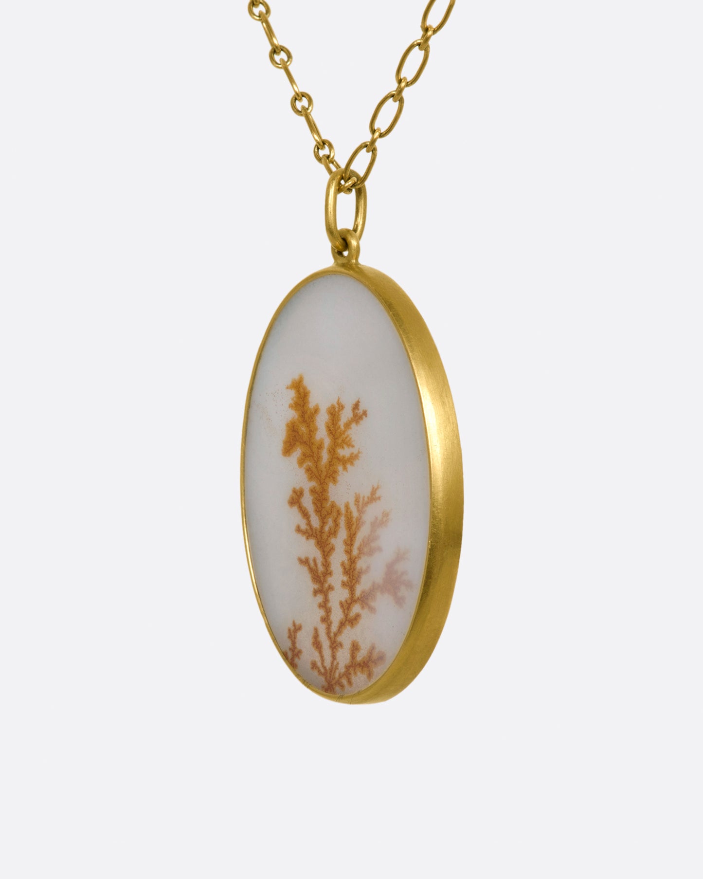 A yellow gold necklace with oval dendritic agate pendant on a yellow gold chain. View up close from the side.