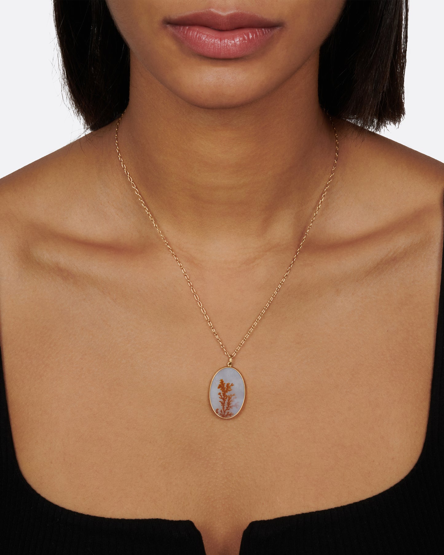 A yellow gold necklace with oval dendritic agate pendant on a yellow gold chain. View on a neck.