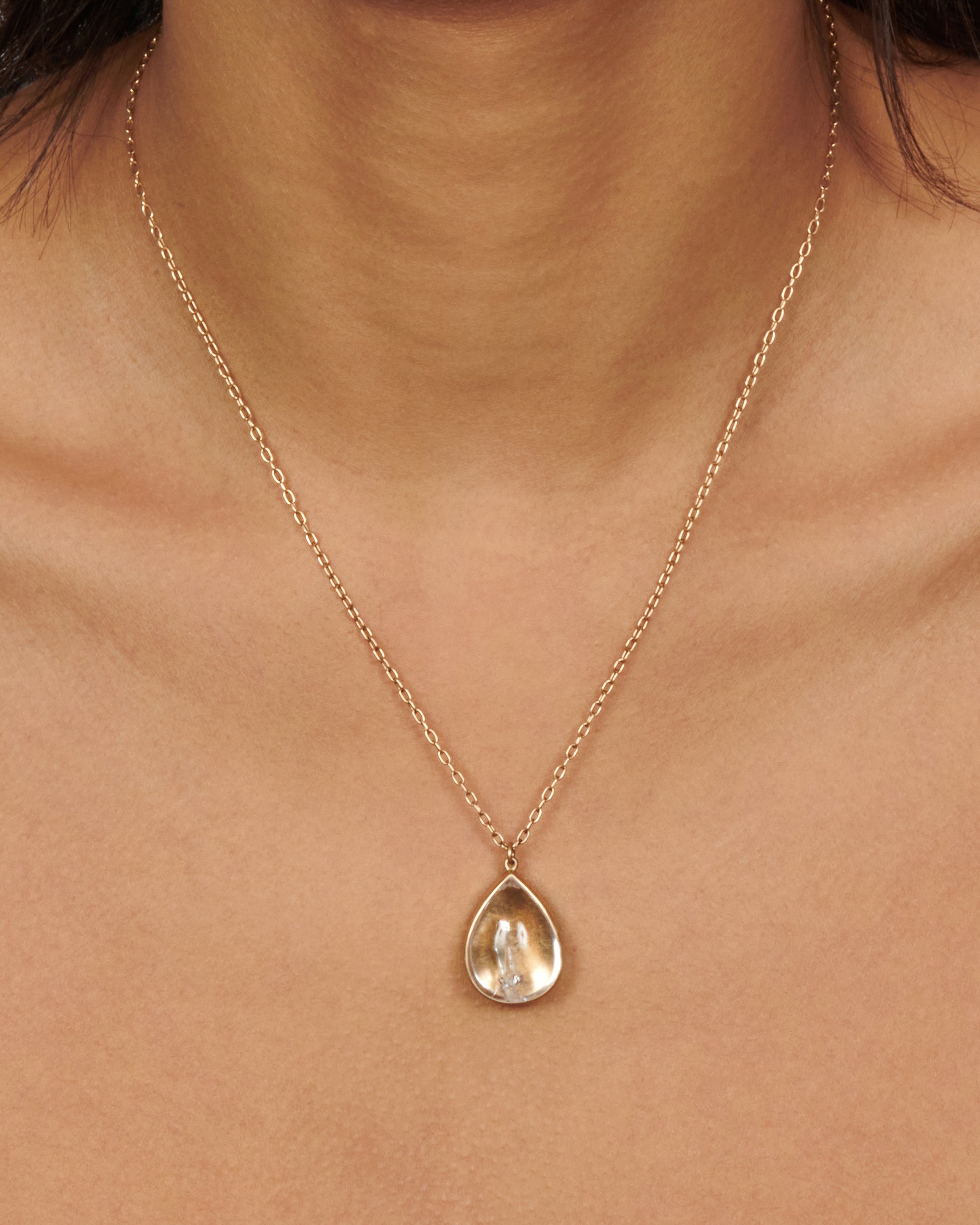 A gold necklace with a quartz crystal teardrop pendant.