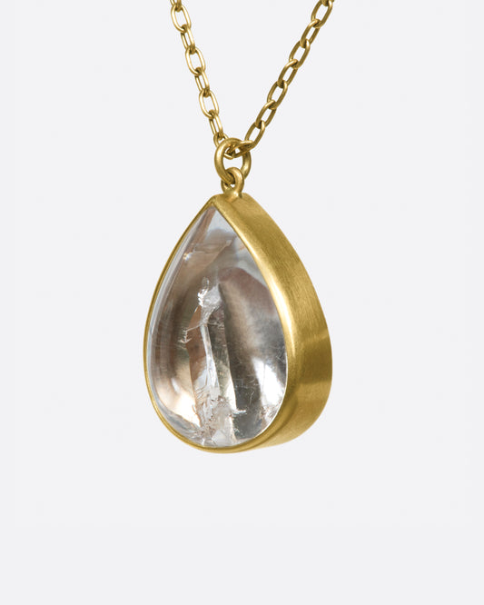 A gold necklace with a quartz crystal teardrop pendant.