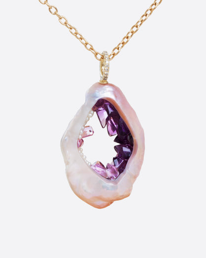 A large soufflé pearl open in the center and filled with pearls and amethysts, hanging from a cable chain and diamond bail. Shown from the front.