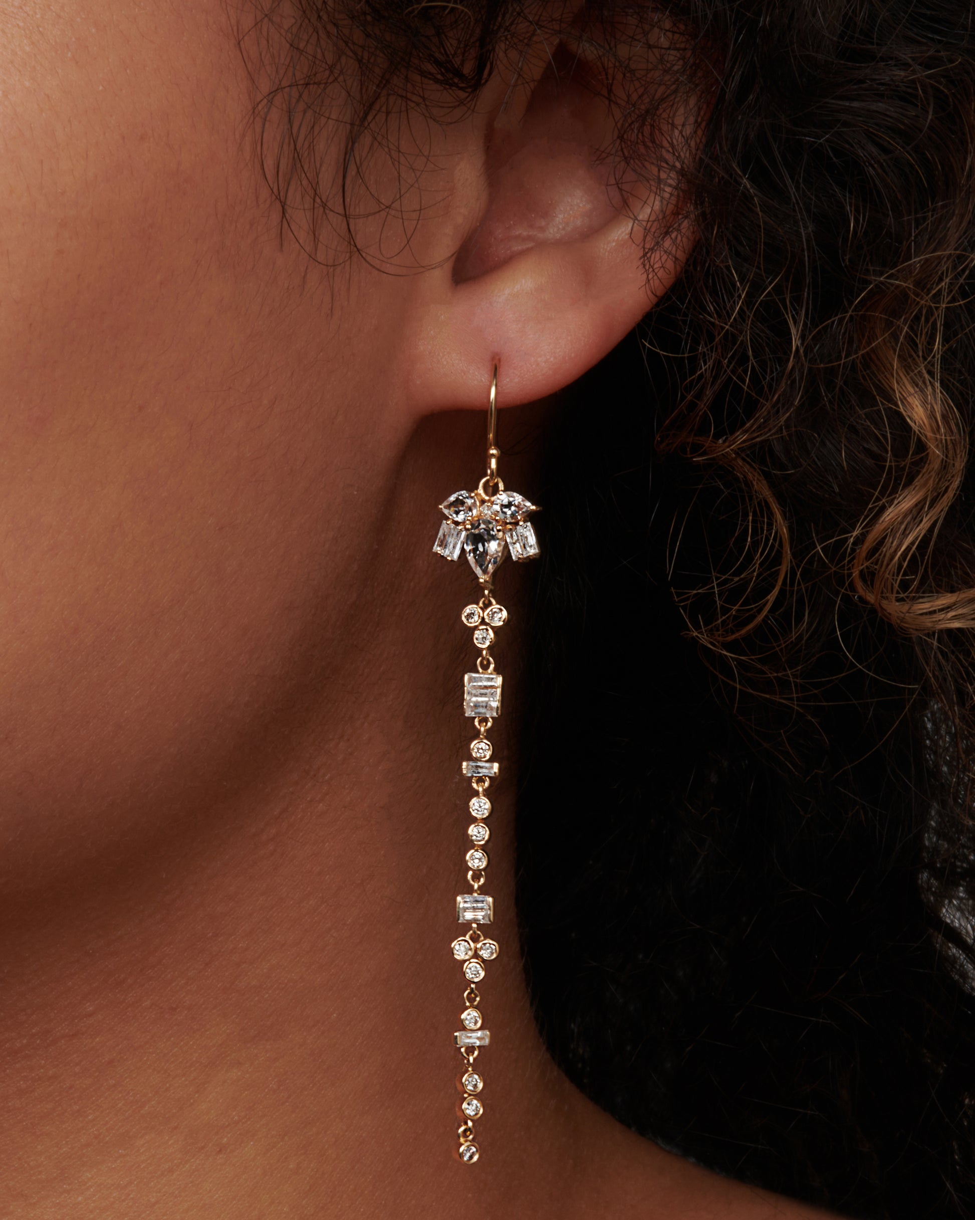 A pair of 14k gold drop earrings with a geometric variety of white topaz and diamonds. View on an ear.