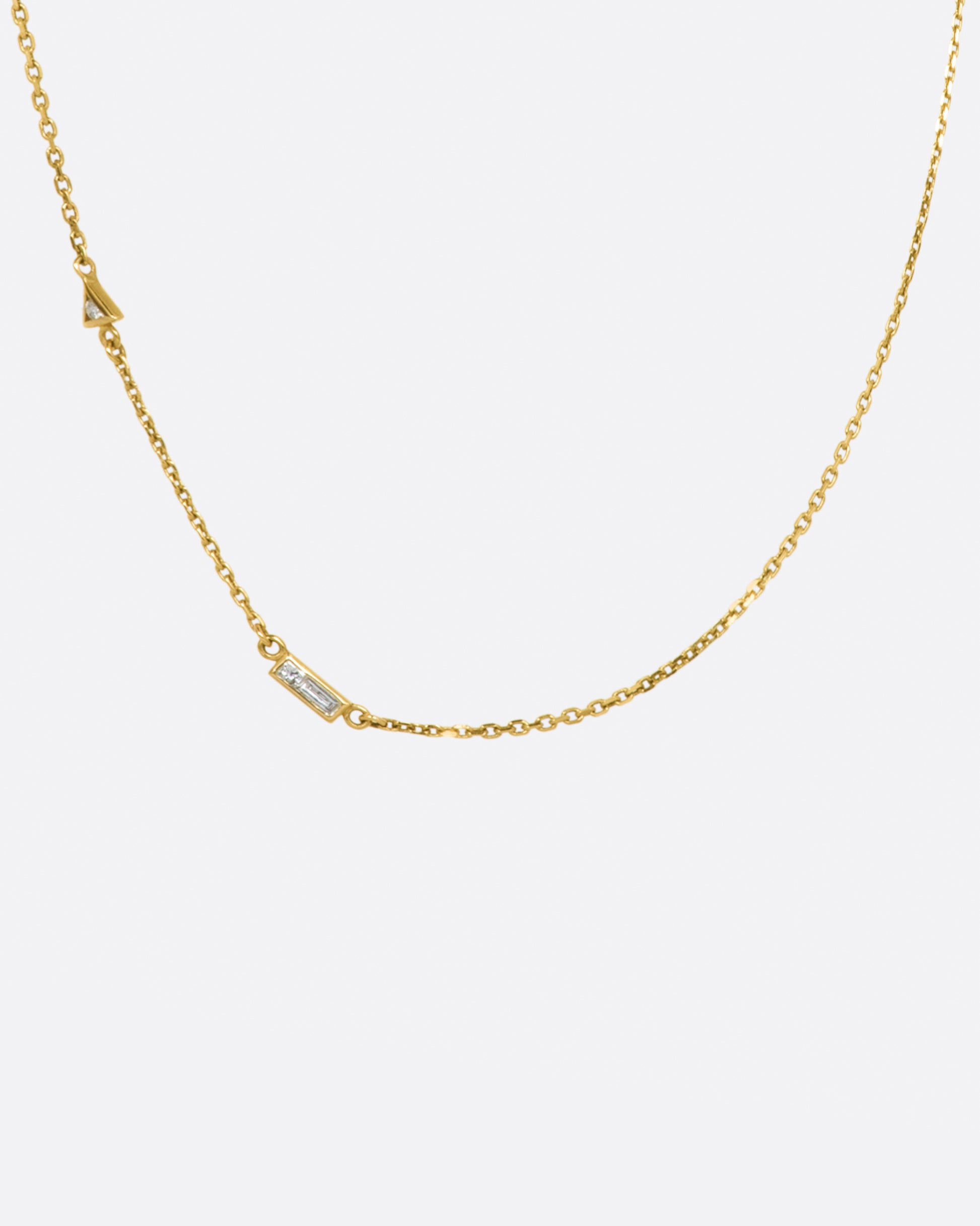 A yellow gold cable chain necklace with a round diamond in a triangular setting and a baguette diamond in a rectangular setting, set into the chain about an inch apart.