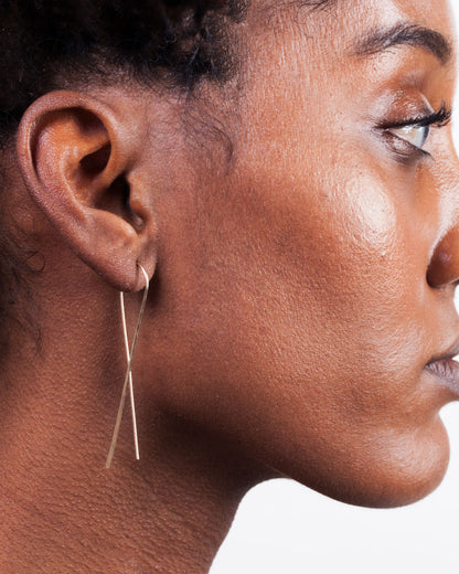Gold wire crossed hook earrings worn on an ear