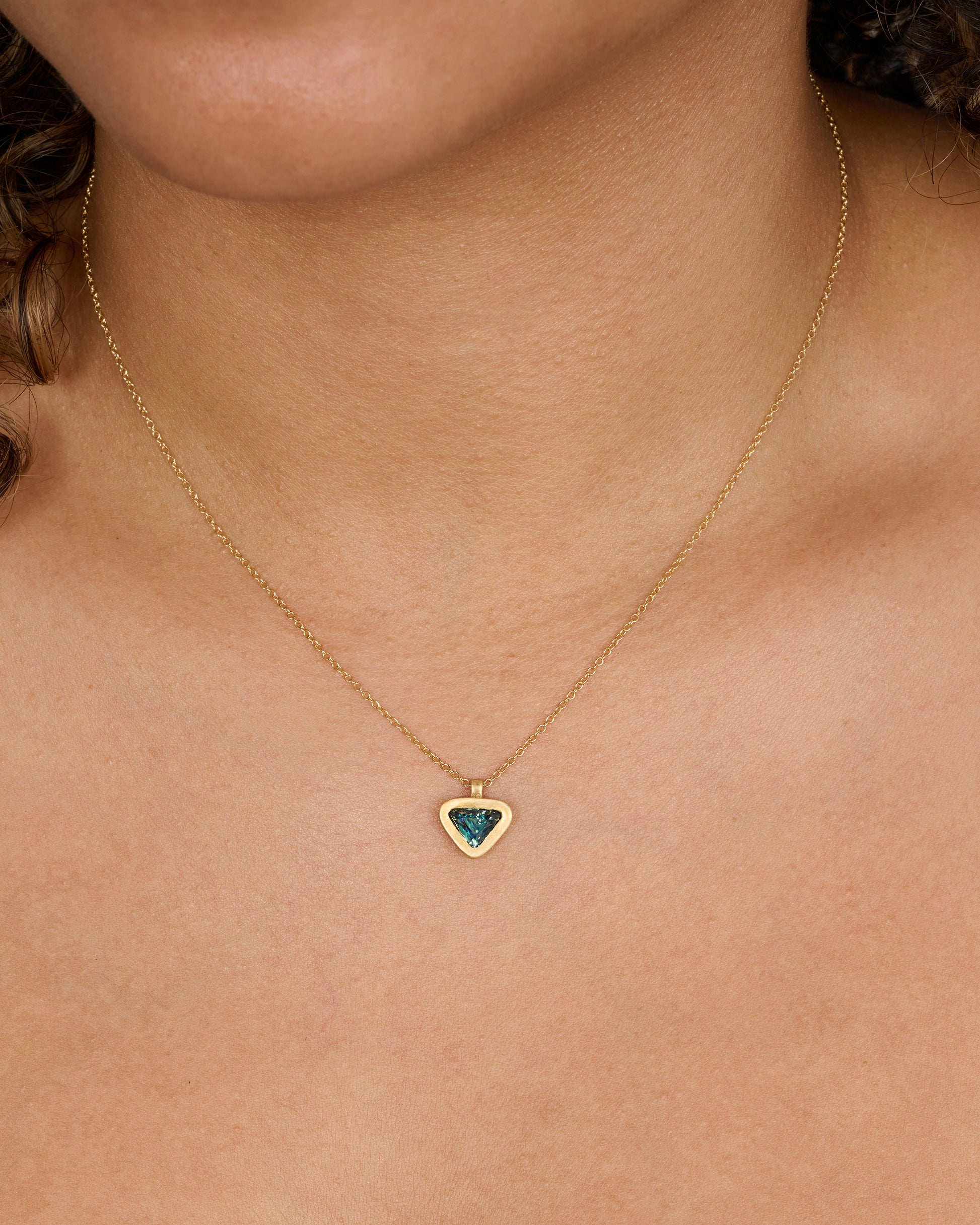 A yellow gold pendant with a triangle green sapphire pendant. Shown on a neck.