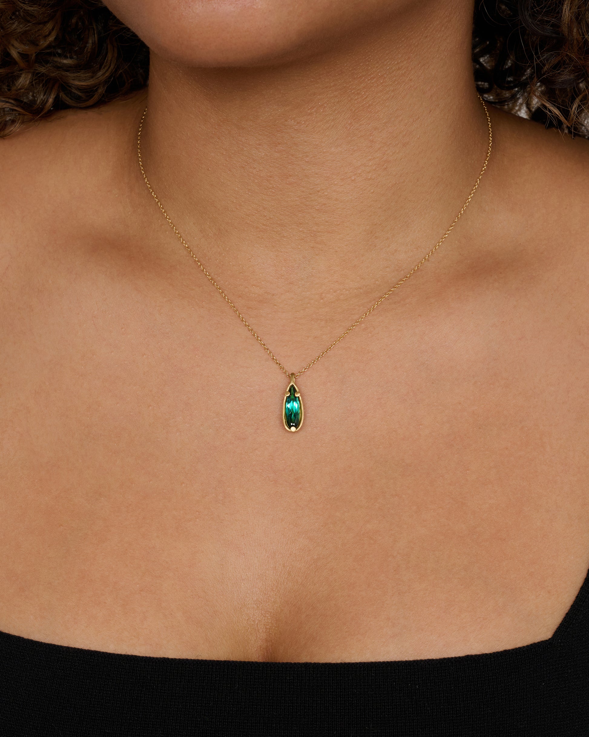 A matte yellow gold necklace with a large pear shaped teal tourmaline pendant. View worn.