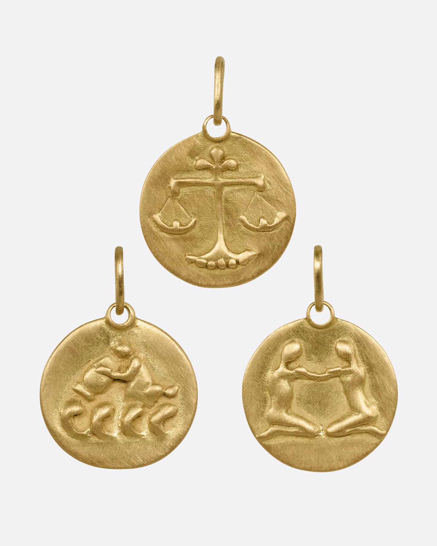 Three circular yellow gold zodiac pendants- one Libra, one Aquarius, and one Gemini, shown from the front.