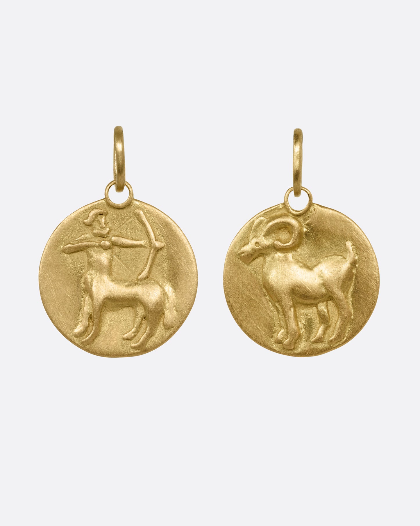 Two yellow gold circular zodiac pendants- one Aries, the other Sagittarius, shown from the front.