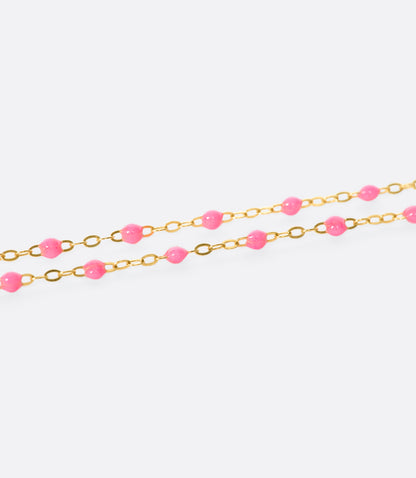 A close up view of a yellow gold cable chain bracelet with neon pink resin droplets. 