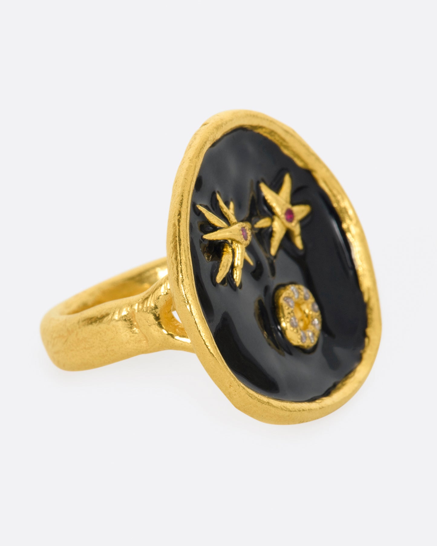 A large high karat gold ring with a round black enamel face, ruby star eyes and a open mouth covered in diamonds. Shown from the side.