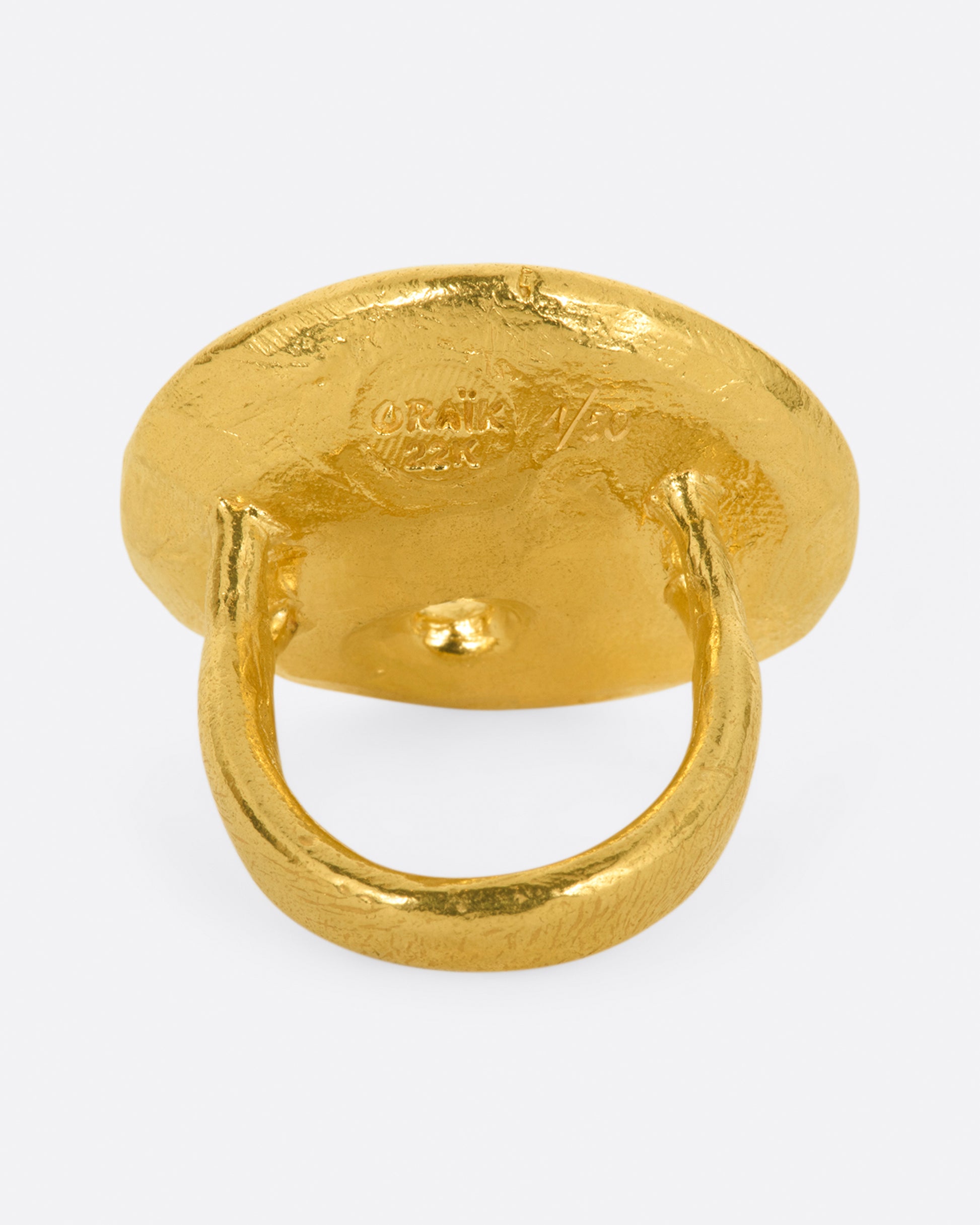 A large high karat gold ring with a round black enamel face, ruby star eyes and a open mouth covered in diamonds. Shown from the back.