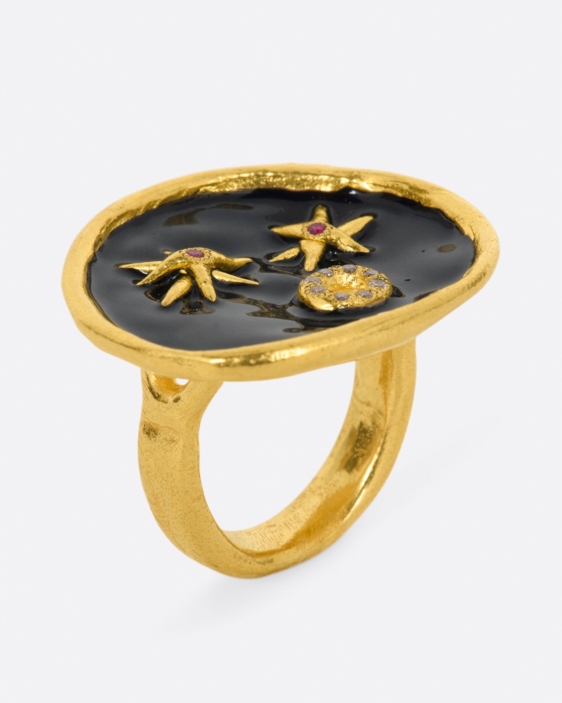 A large high karat gold ring with a round black enamel face, ruby star eyes and a open mouth covered in diamonds. Shown from the side.