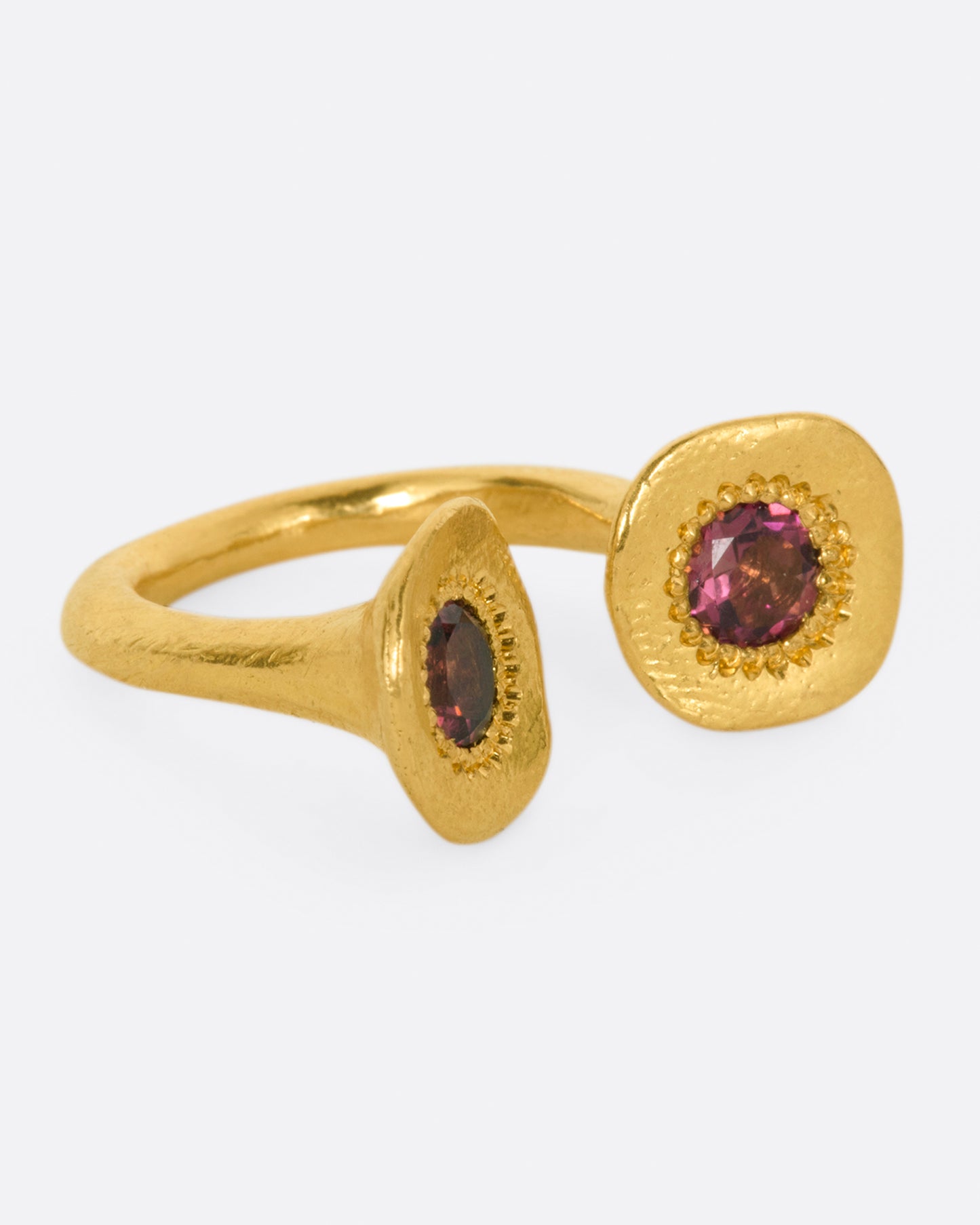 A high karat gold open ring with a large organic shaped disc on each end with a rosey pink tourmaline at its center. Shown from the side.