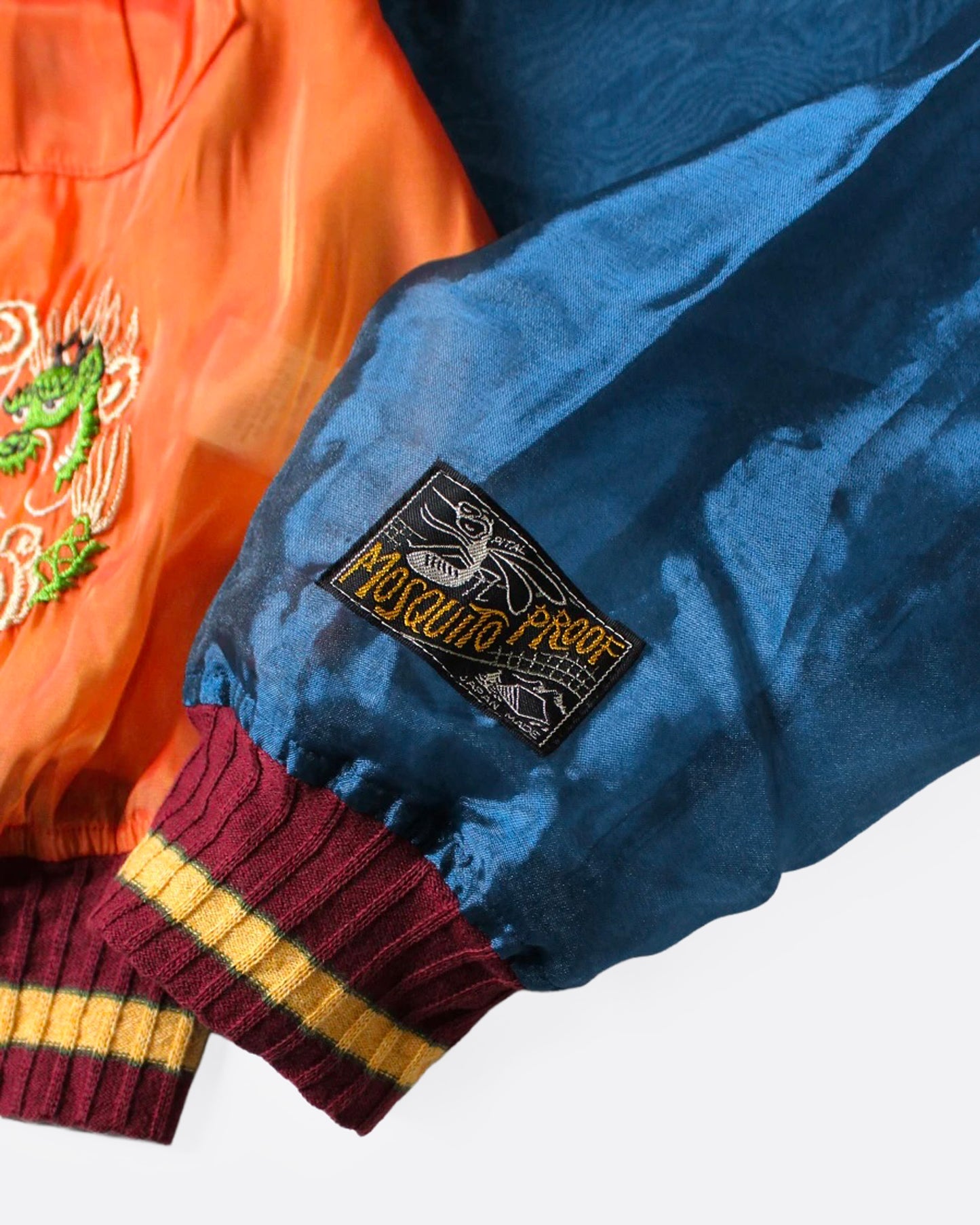 A close up of the sleeve of an orange and blue sheer bomber jacket with dragon embroidery.