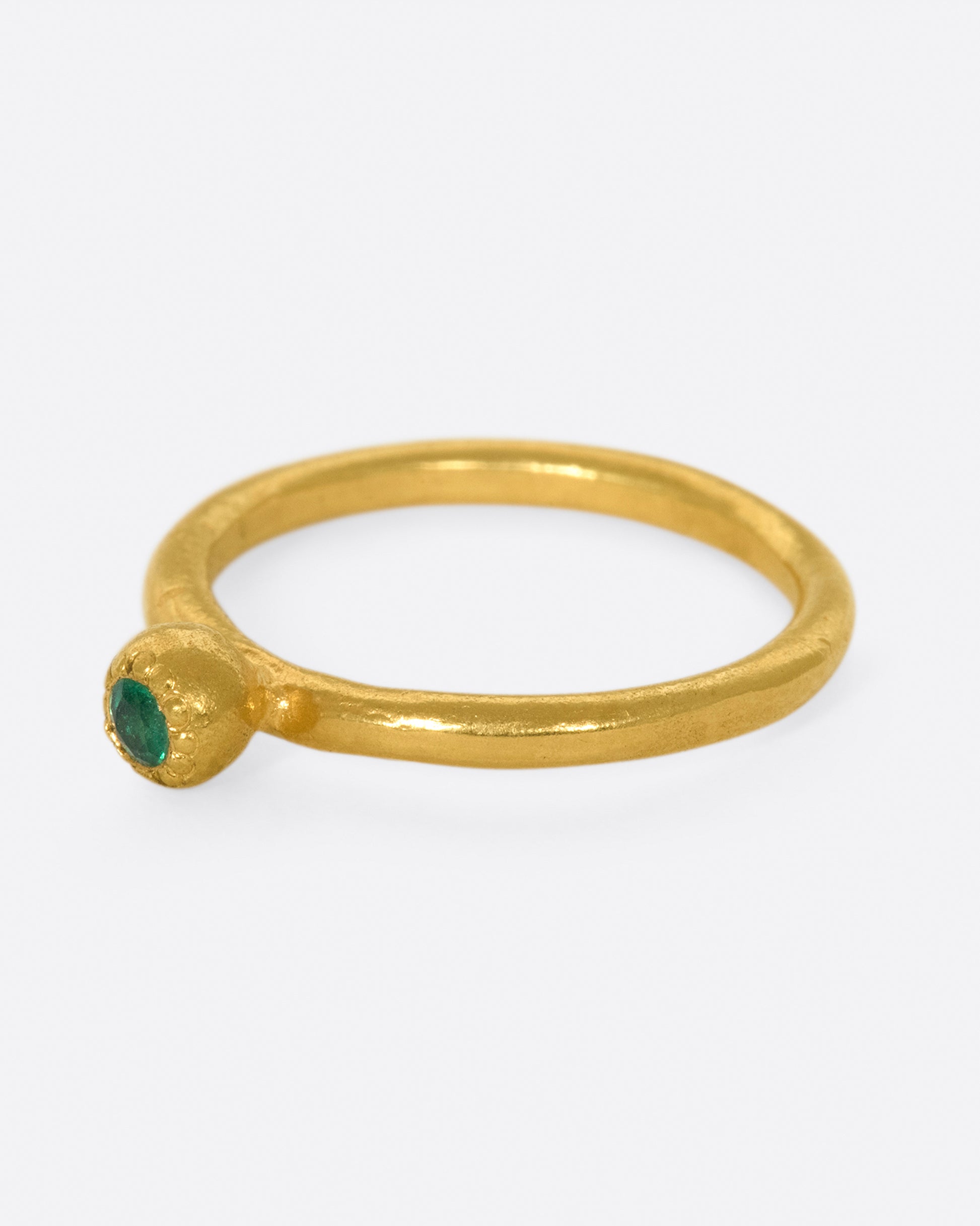 A hand sculpted, high karat gold, solitaire ring with an emerald at its center.