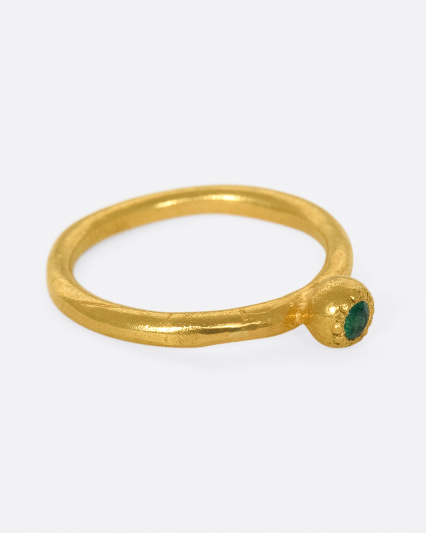 A hand sculpted, high karat gold, solitaire ring with an emerald at its center.