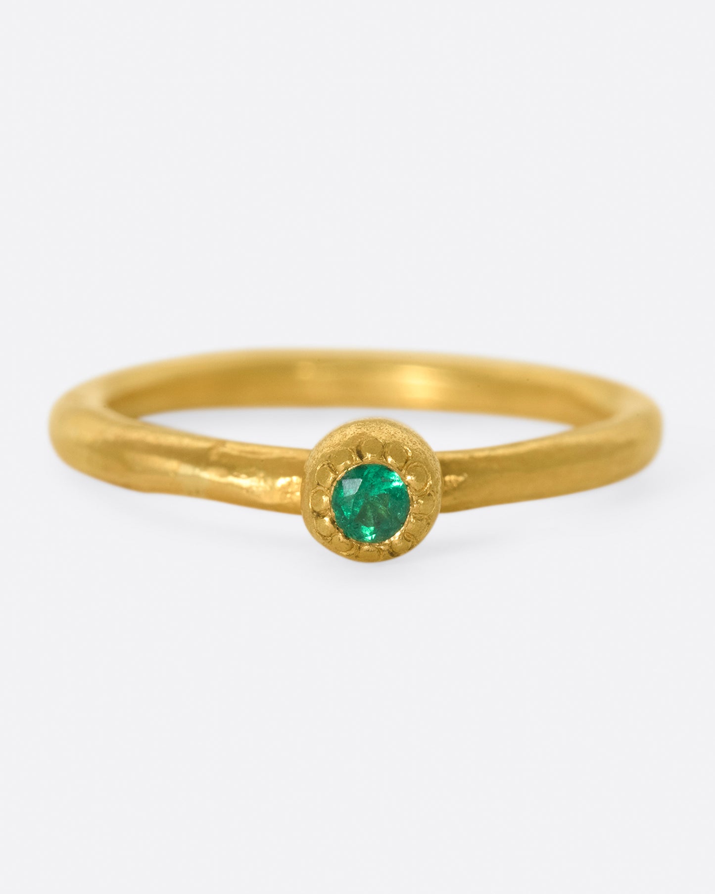 A hand sculpted, high karat gold, solitaire ring with an emerald at its center.