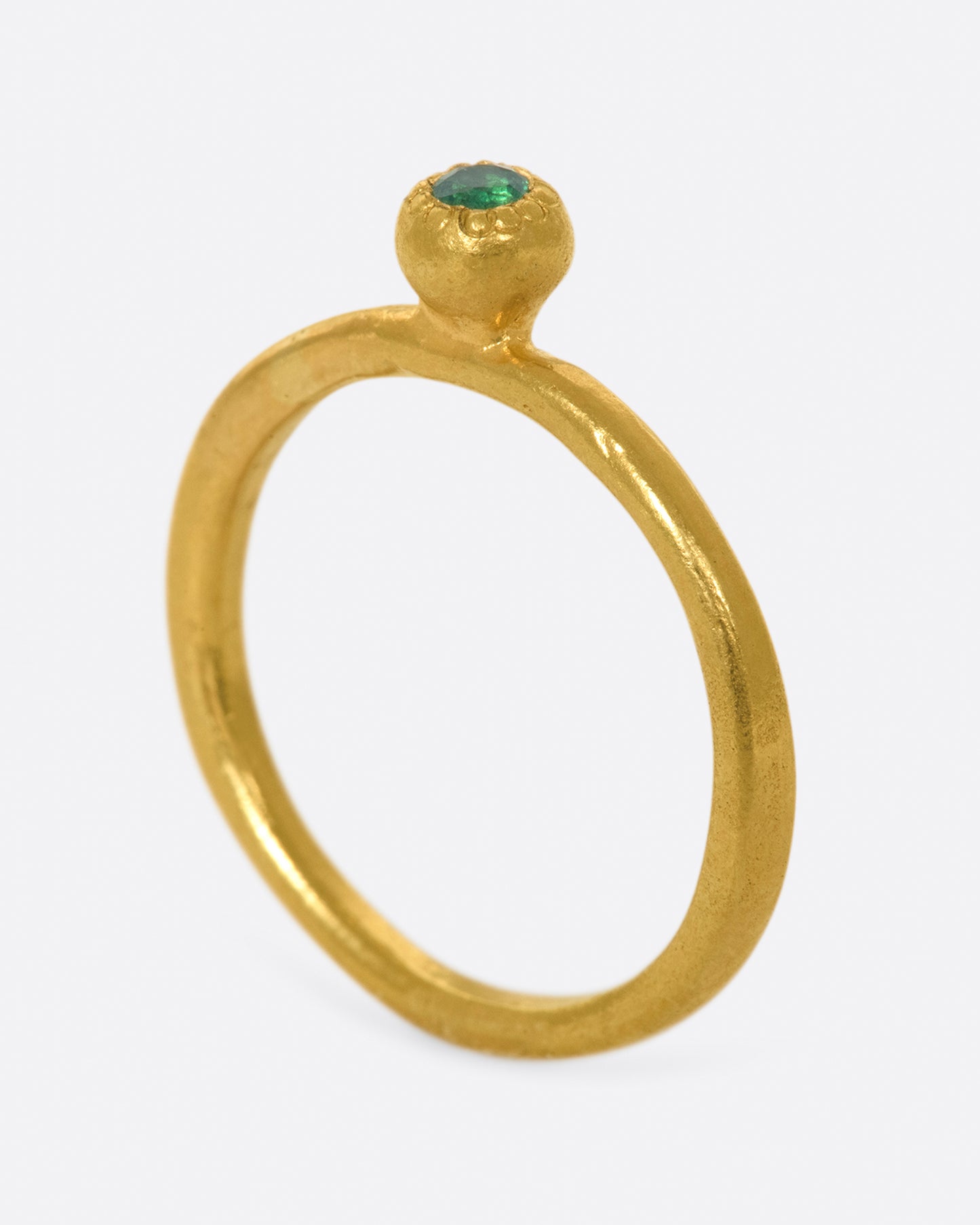 A hand sculpted, high karat gold, solitaire ring with an emerald at its center.