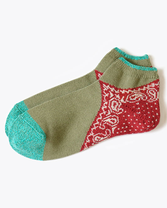 A pair of sage green and turquoise green socks with a red paisley bandana print heel. Shown lying flat from the side.