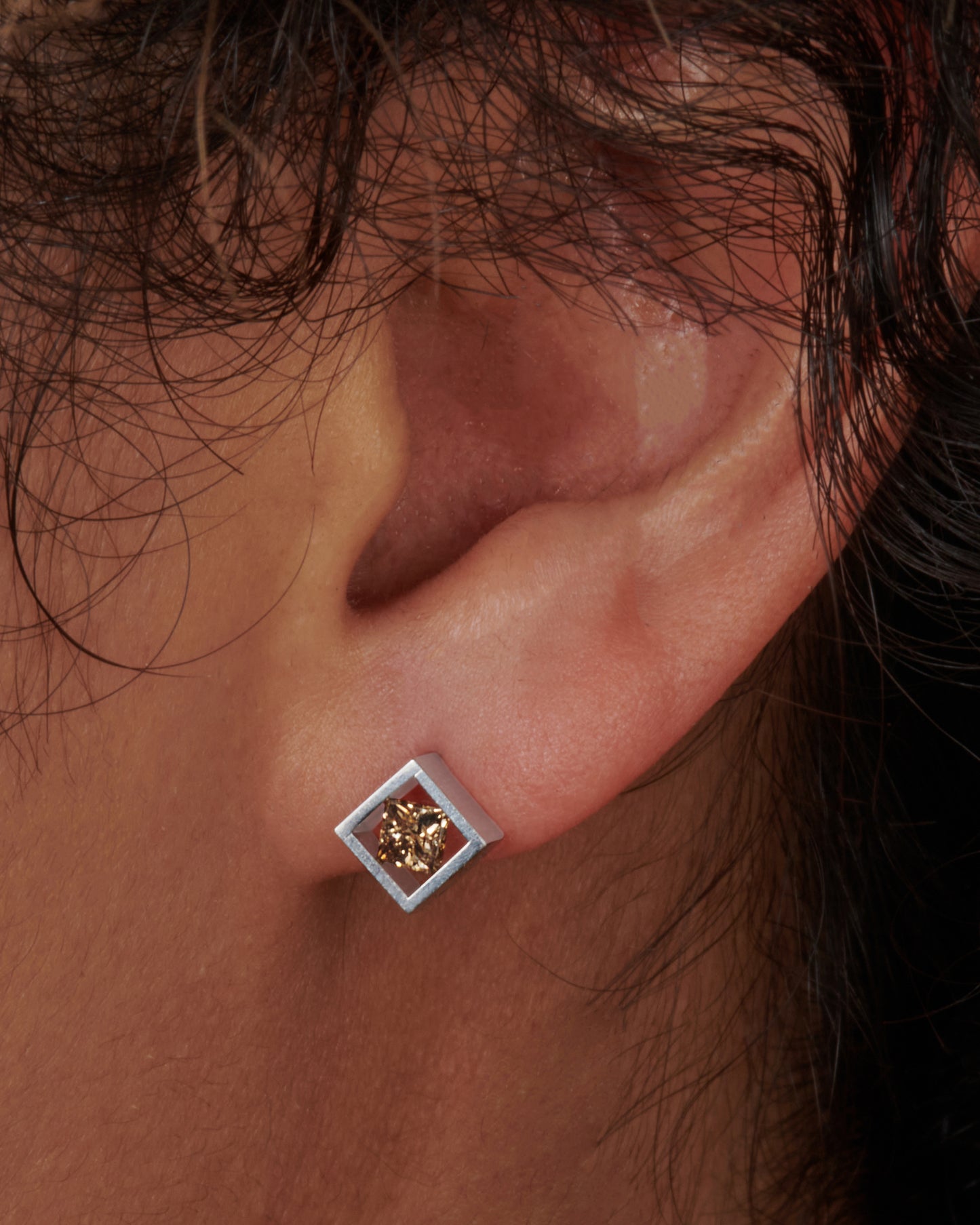 A pair of princess-cut cognac diamonds stretching across a square platinum setting. View on an ear.