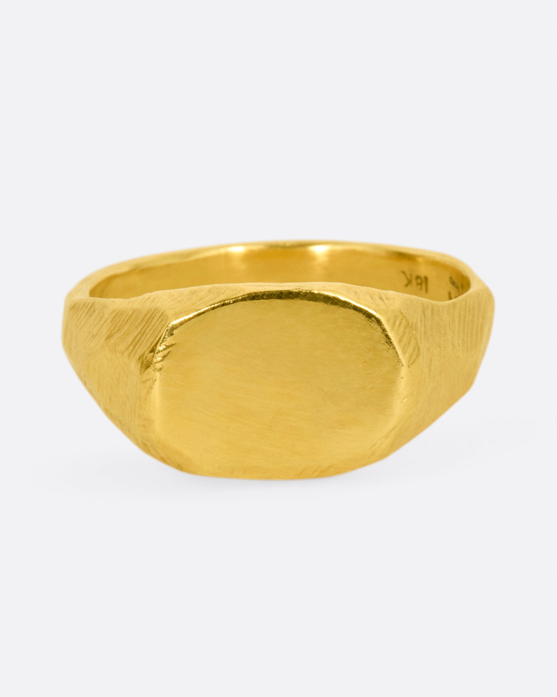 A yellow gold signet ring with a flat, polished face and textured band. Shown from the side.