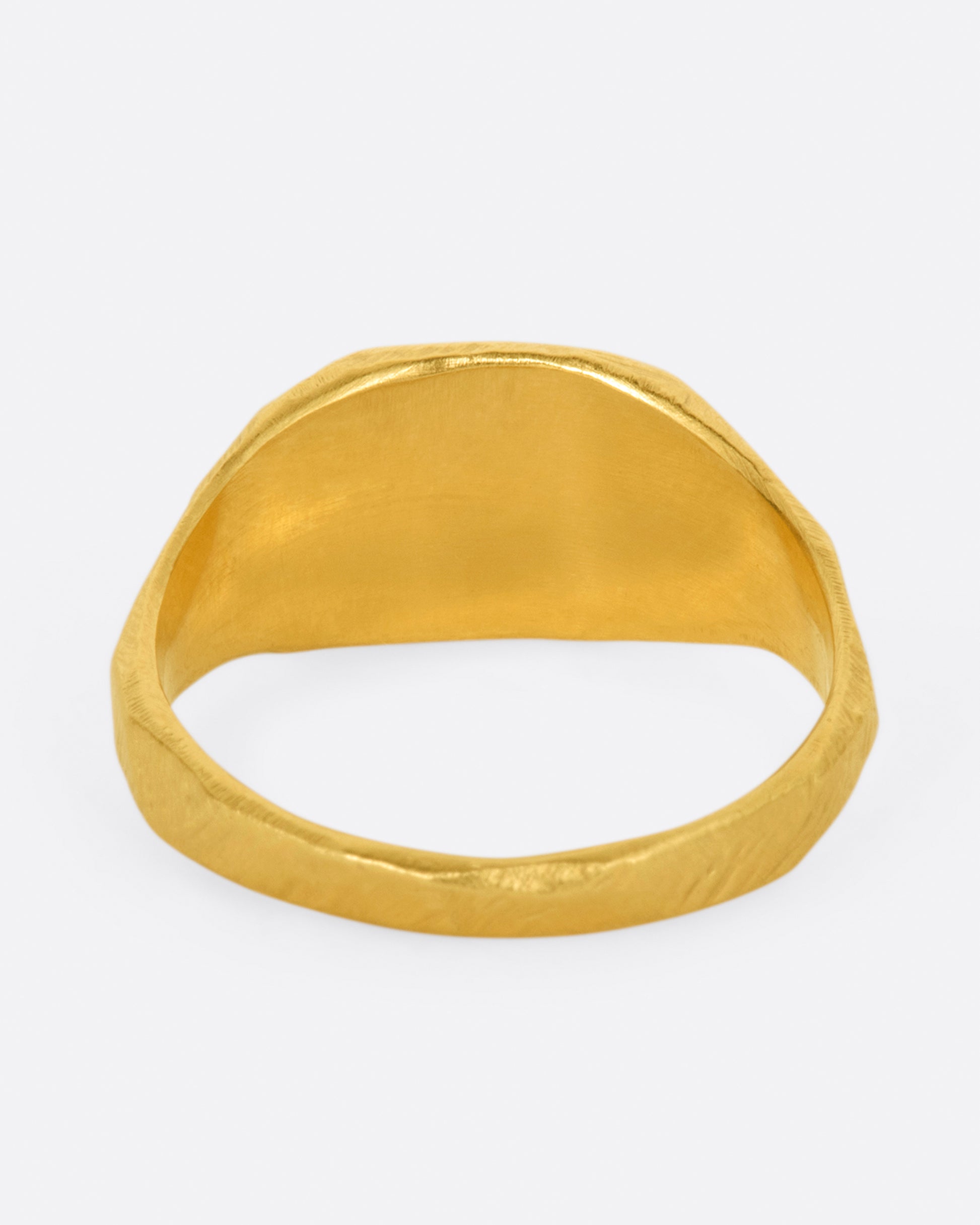 A yellow gold signet ring with a flat, polished face and textured band. Shown from the side.