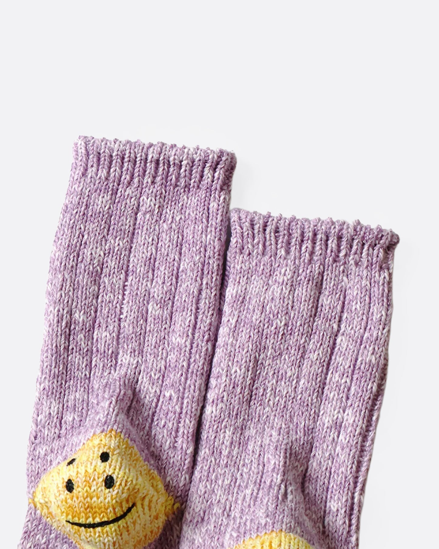 A pair of purple ribbed cotton socks with double-eyed smiley faces on each heel, shown from the bottom close up.