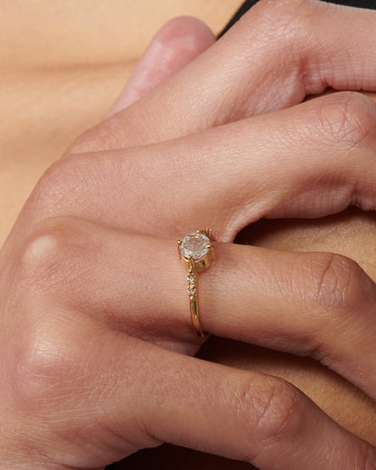 A yellow gold ring with a prong set rose cut diamond at the center and two diamonds on either side, shown from the front on a person.