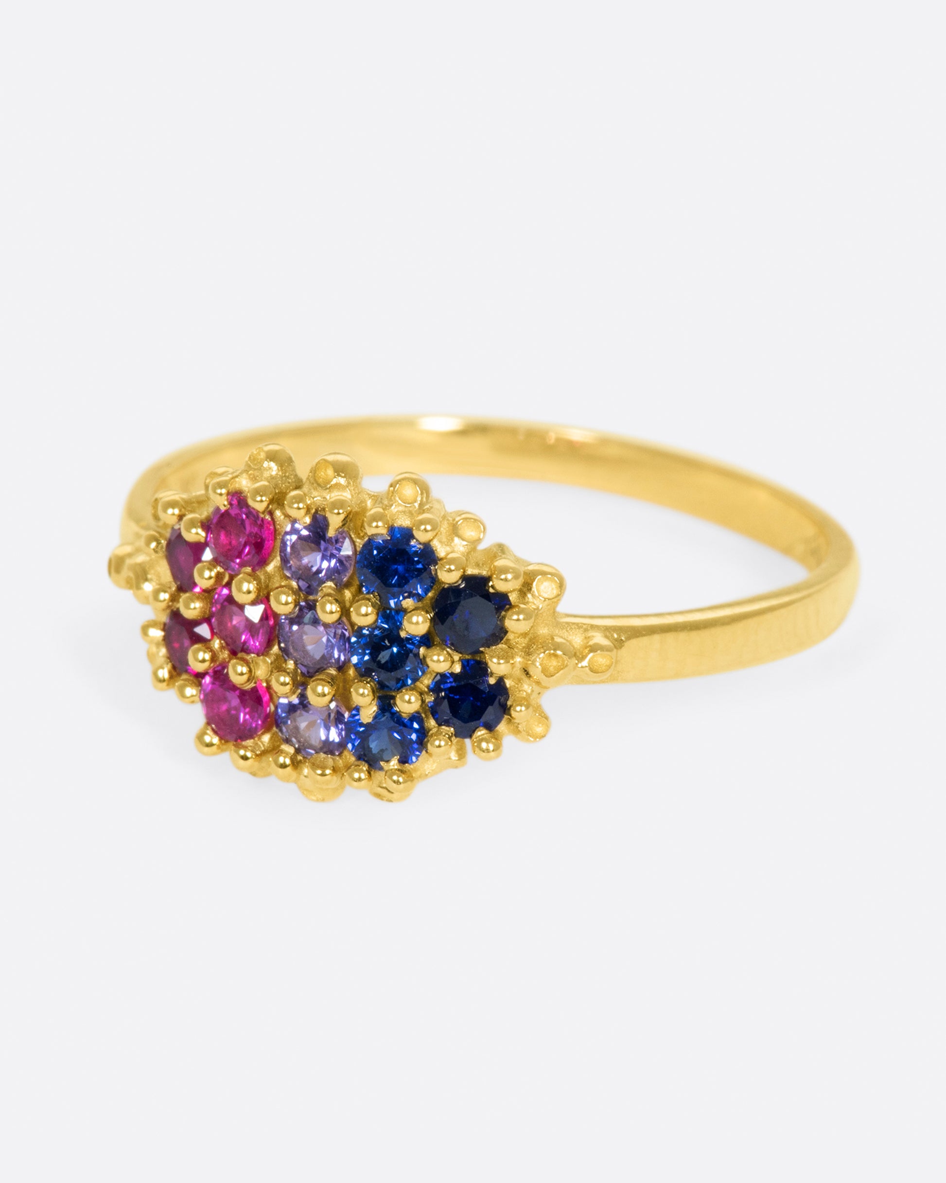 A yellow gold signet style ring whose face is lined with ombré pink to blue sapphires in textured prong settings. Shown from the side.