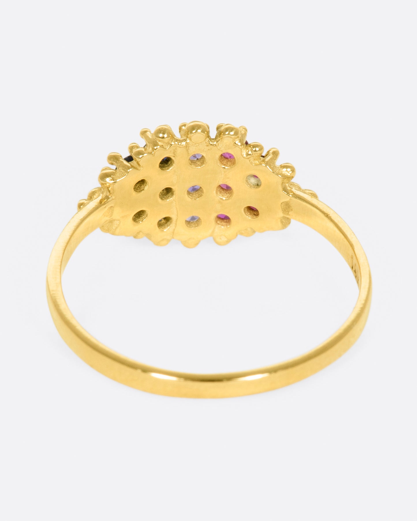 A yellow gold signet style ring whose face is lined with ombré pink to blue sapphires in textured prong settings. Shown from the back.