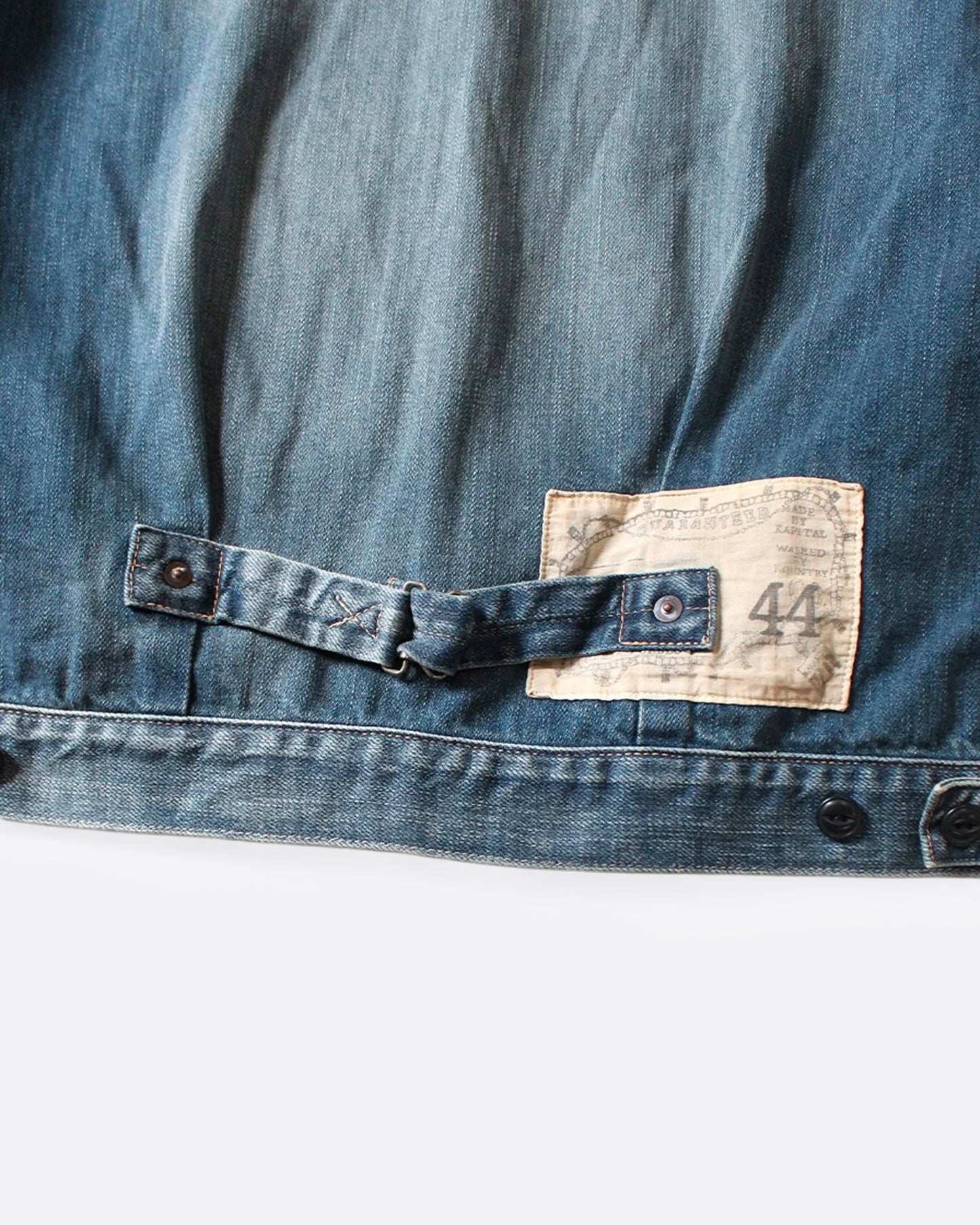 A close up of the back cinch of a light blue denim jacket.