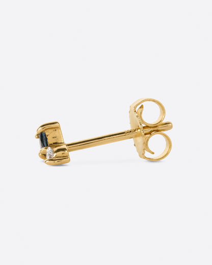 A yellow gold stud earring with a prong set round diamond sitting atop a princess cut teal blue sapphire. Shown on its side from the side.