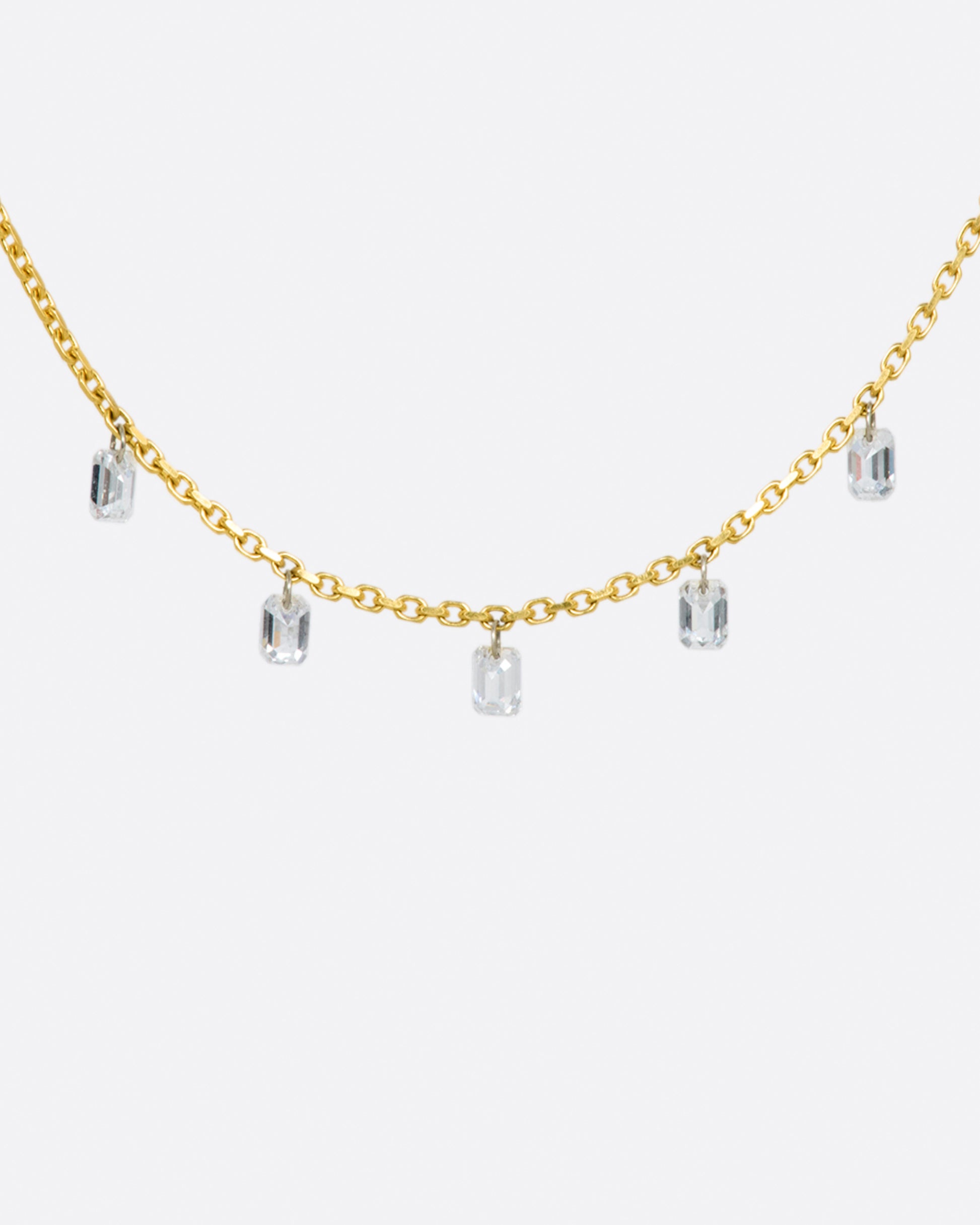 A yellow gold chain necklace with five free set dangling emerald cut diamonds spaced about half an inch apart from one another.