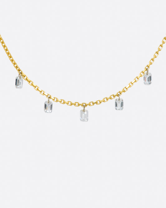 A yellow gold chain necklace with five free set dangling emerald cut diamonds spaced about half an inch apart from one another.