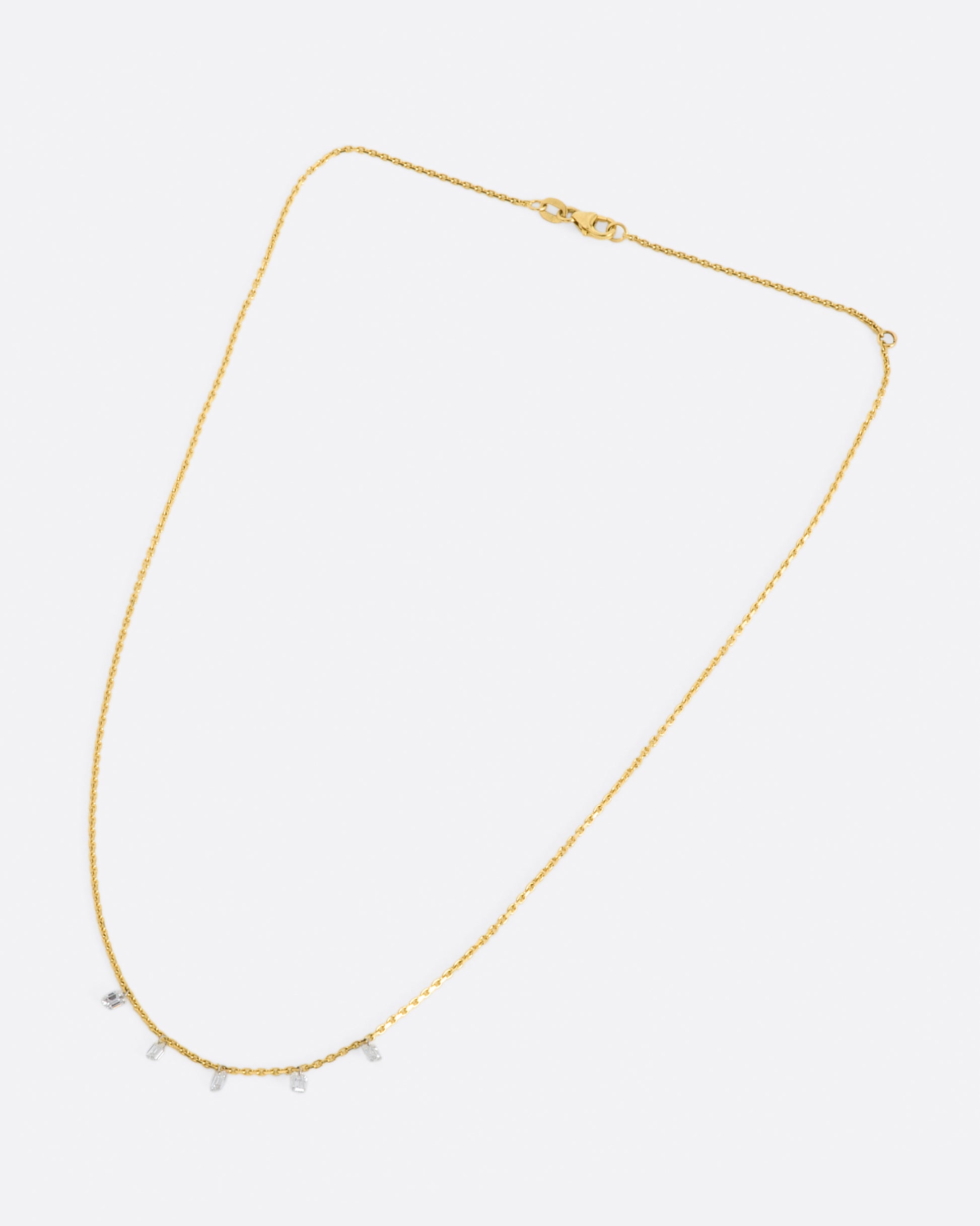 A yellow gold chain necklace with five free set dangling emerald cut diamonds spaced about half an inch apart from one another.