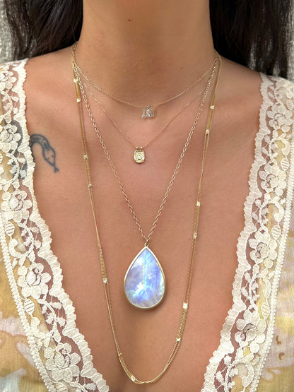 Yellow gold moonstone teardrop necklace worn layered with fine gold necklaces, glowing blue in the light