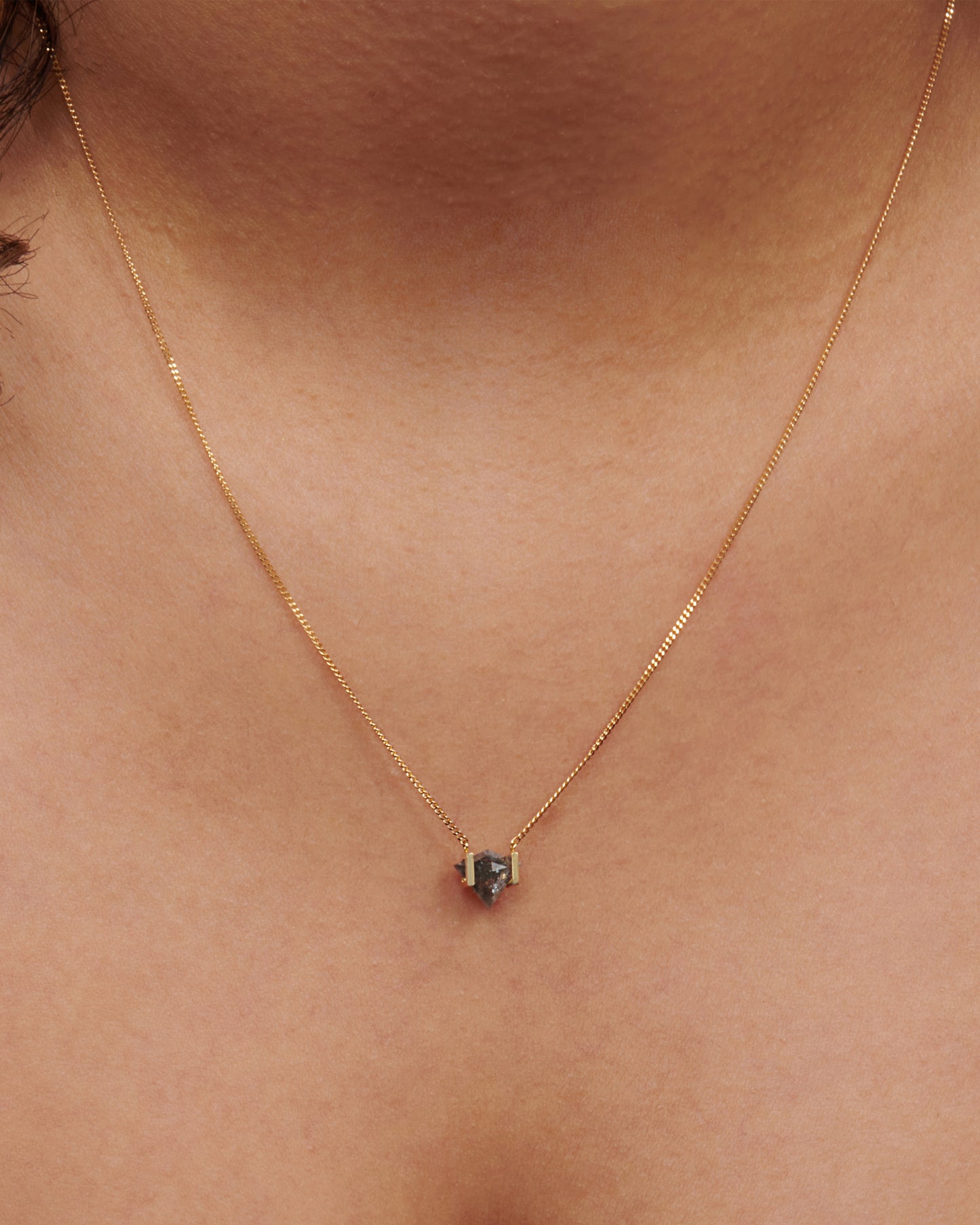 A diamond-shaped salt and pepper diamond suspended between two 18k gold bar. View on a neck.