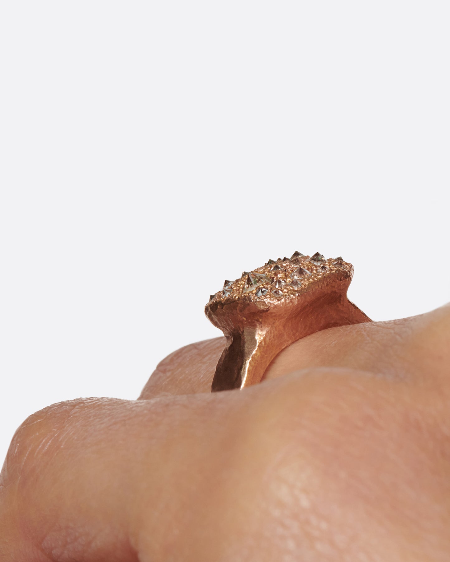 A hammered, hefty rose gold ring with inverted diamonds scattered across its rectangular face.