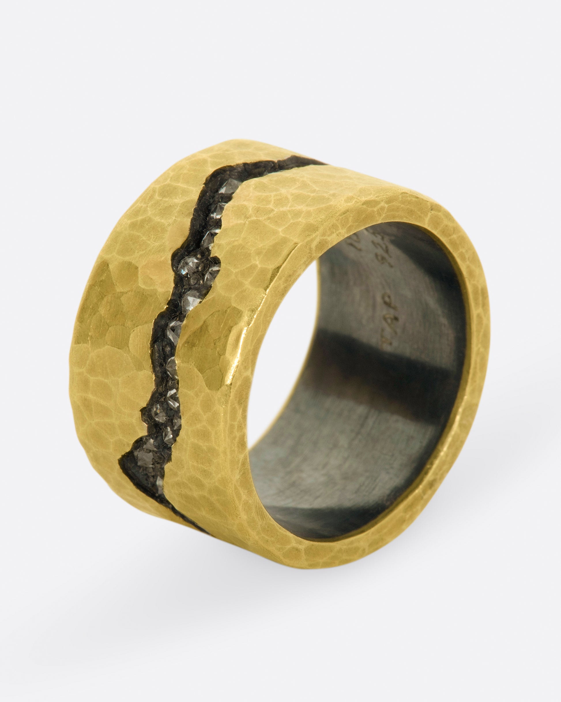 A wide sterling silver band ring with a layer of hammered 18k yellow gold on top and a fissure all the way around that's lined with inverted diamonds.