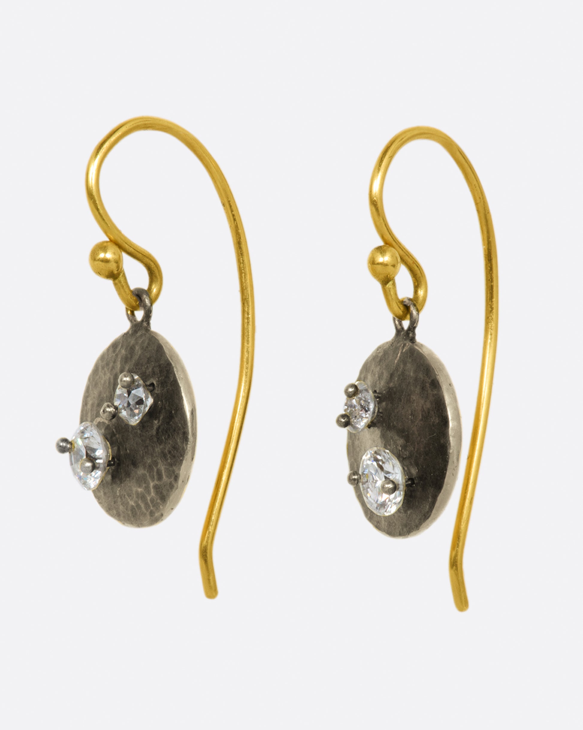 A pair of white gold hammered circle drop earrings with two round diamonds on each, yellow gold ear wires and yellow gold backsides.