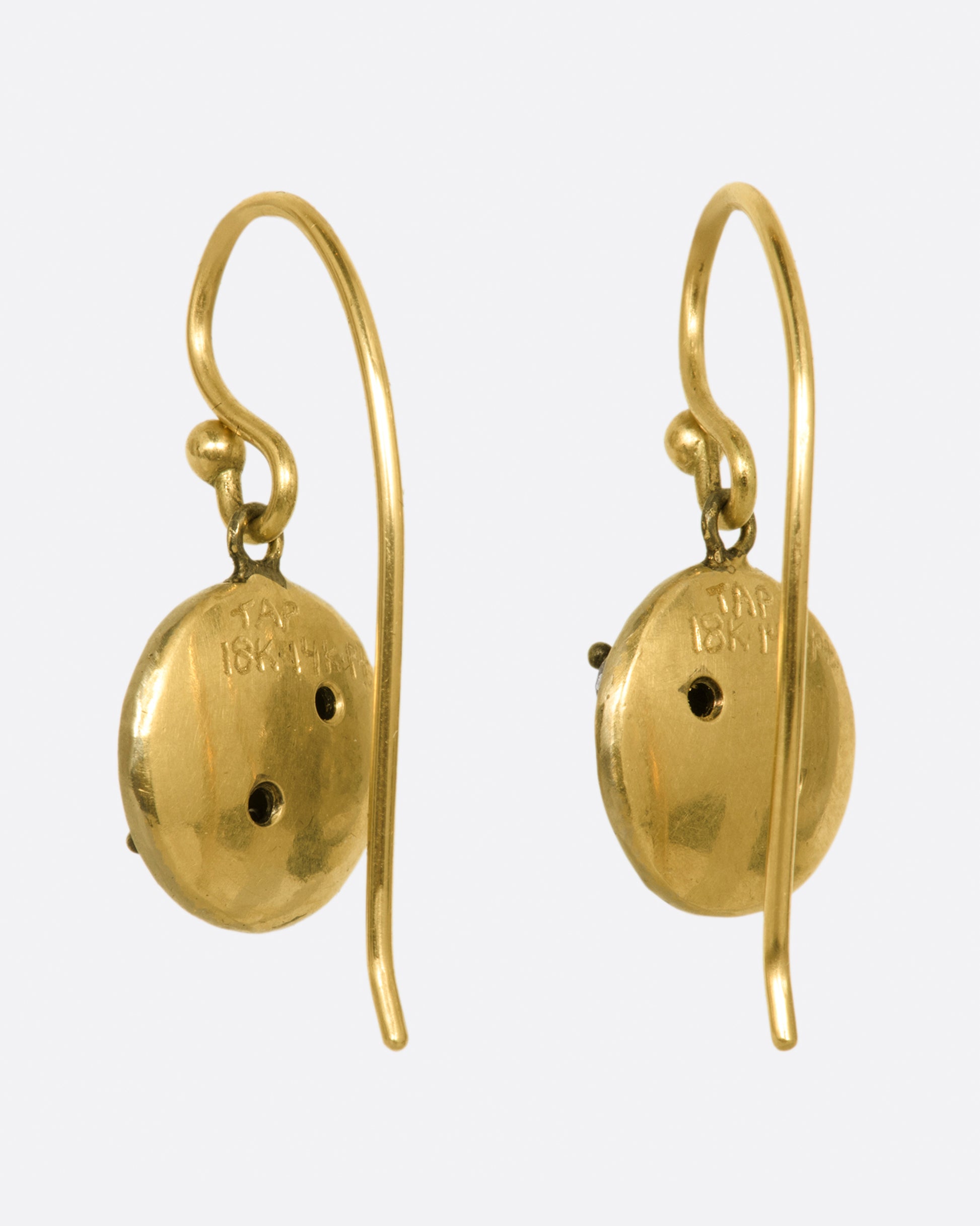 A pair of white gold hammered circle drop earrings with two round diamonds on each, yellow gold ear wires and yellow gold backsides.