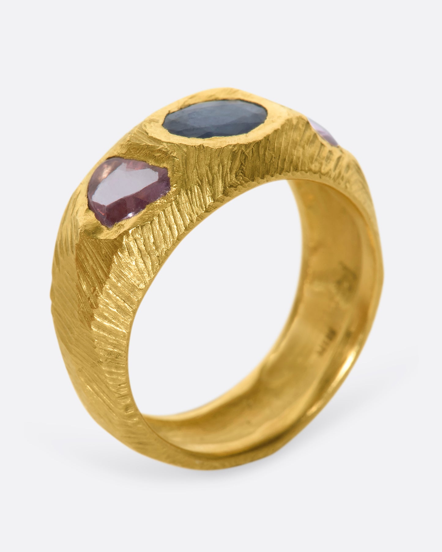 This hand carved 18k gold band is inlaid with an oval blue sapphire, flanked by beautiful pink sapphires