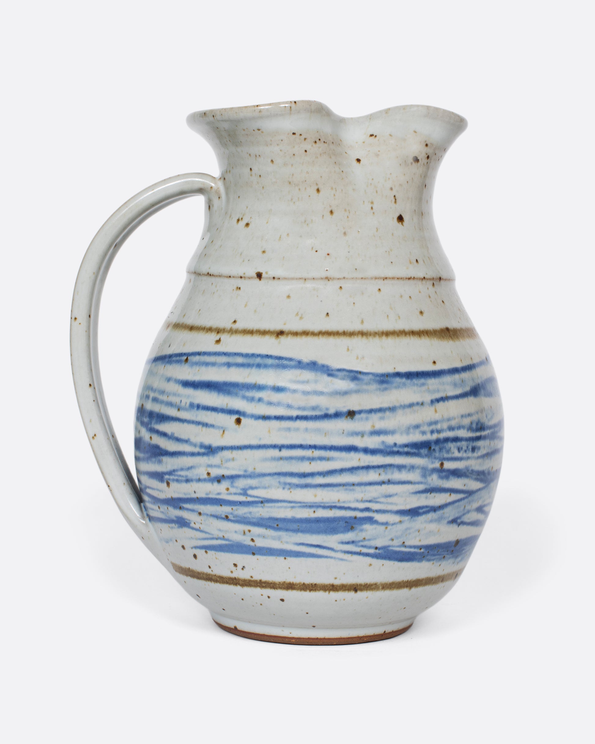 This vintage studio-made ceramic pitcher features a speckled white glaze and a blue water-like, hand-painted pattern.