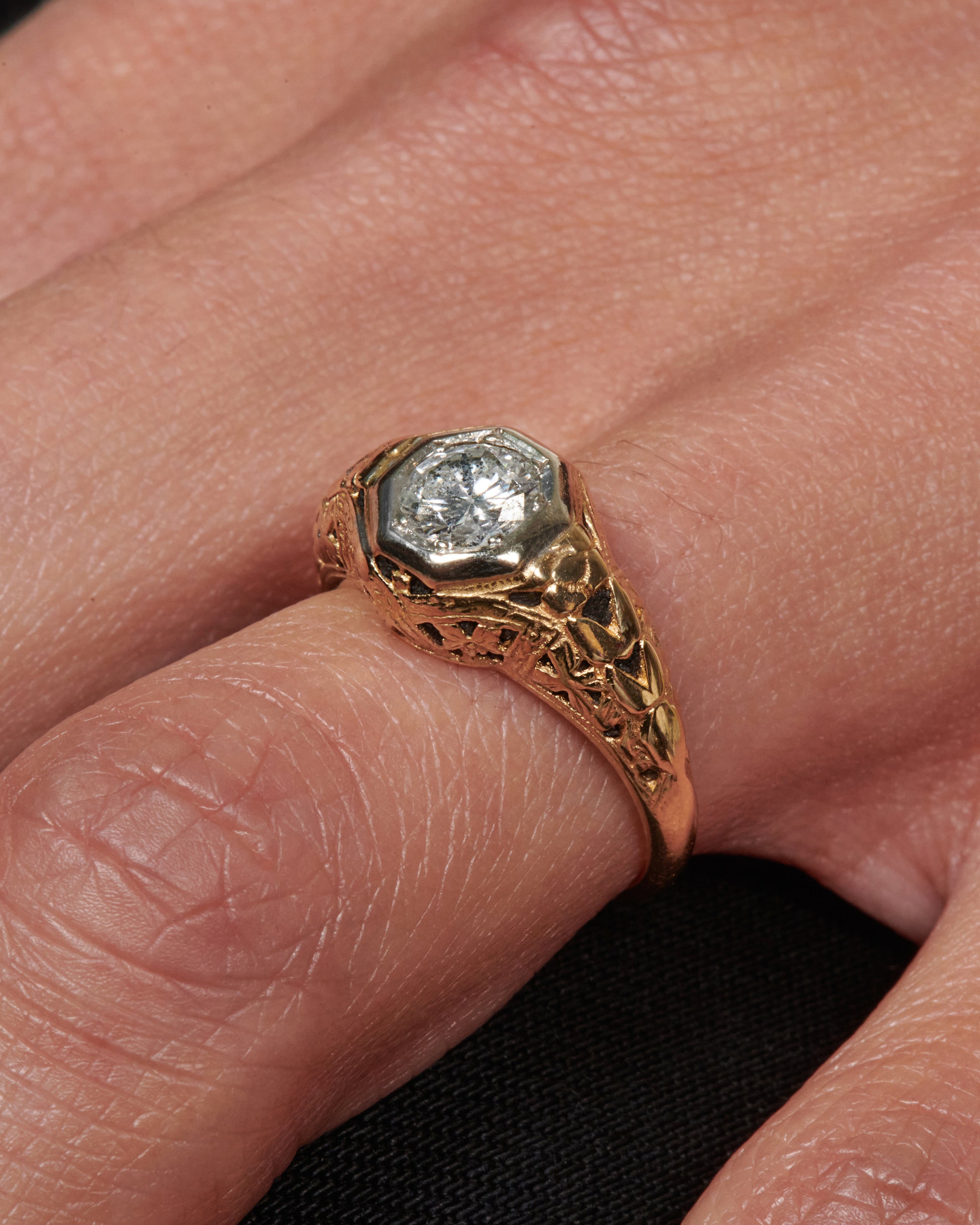 A filigree-covered signet ring with a champagne diamond at its center, set in a white gold bezel.