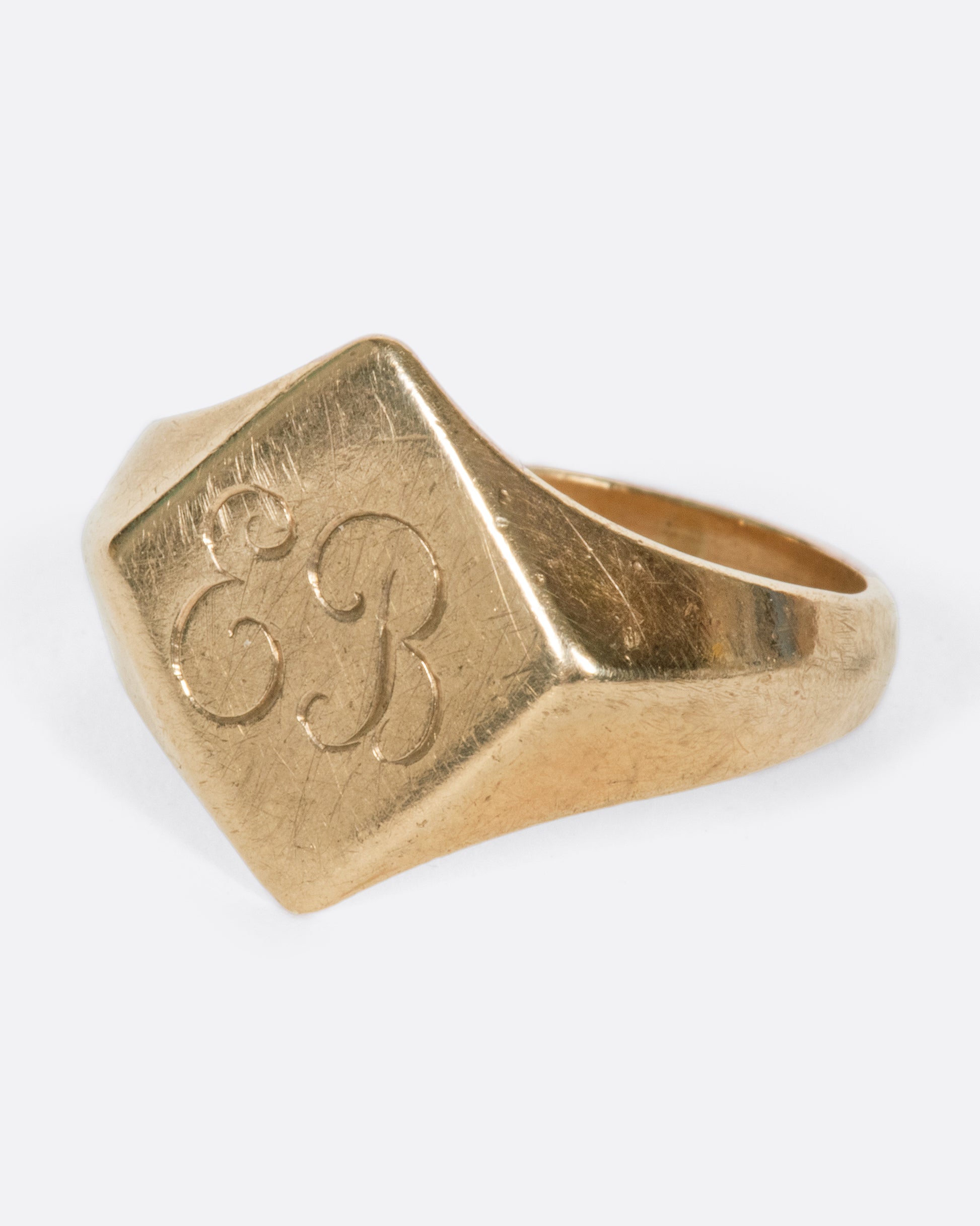 A vintage yellow gold signet ring with a diamond shaped face and the initials EB engraved on the front.