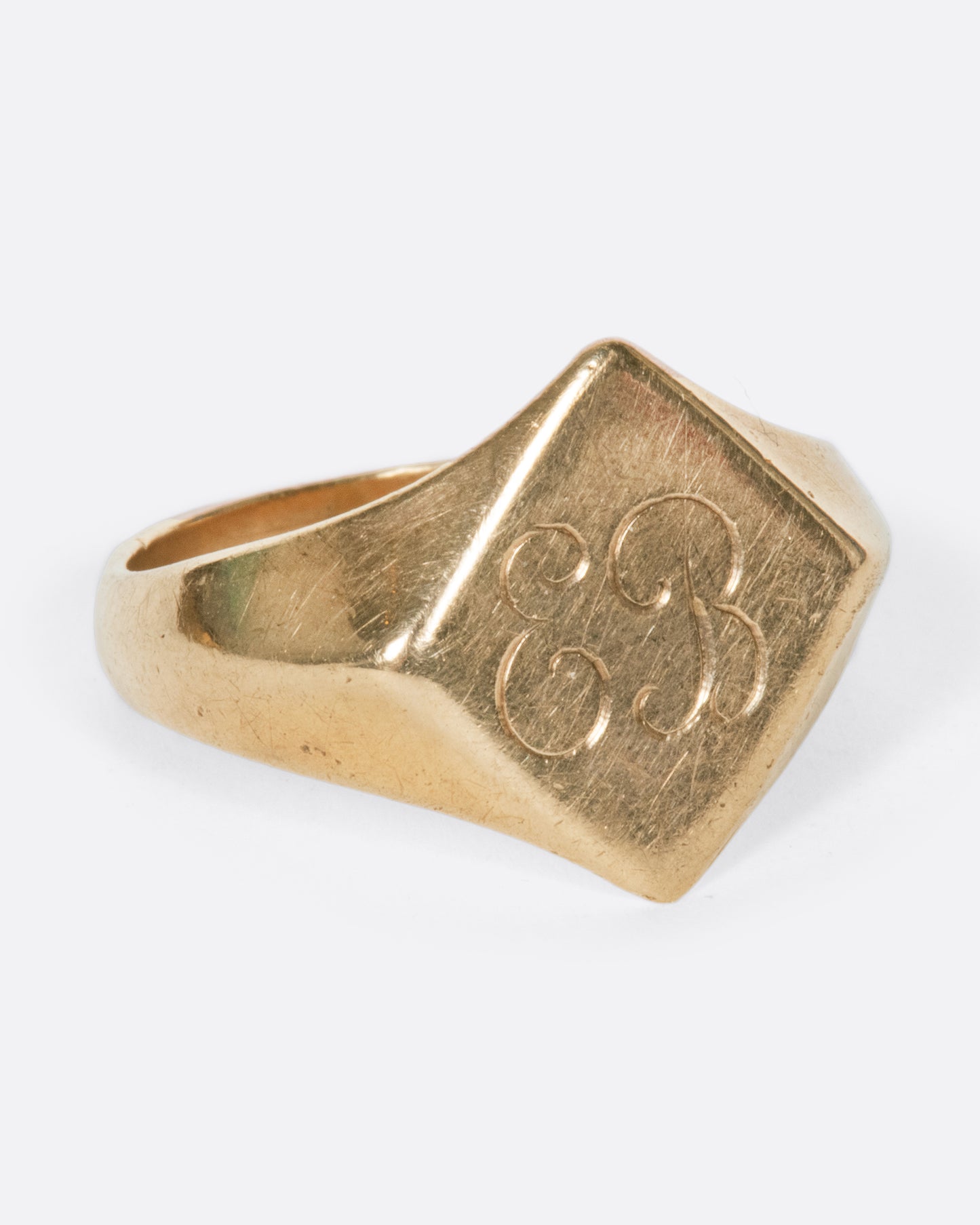 A vintage yellow gold signet ring with a diamond shaped face and the initials EB engraved on the front.