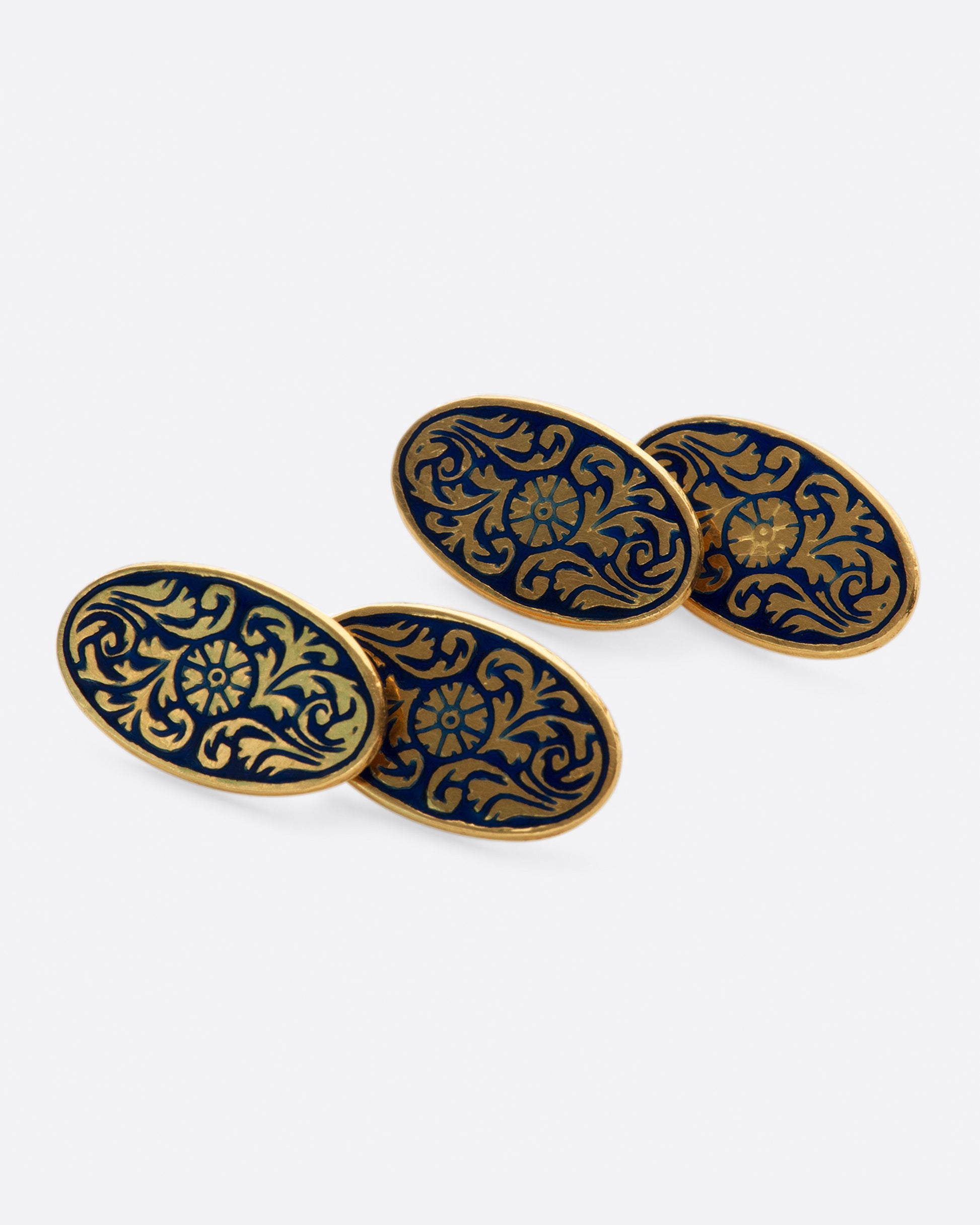 A pair of solid gold vintage cufflinks with intricate flourishes and contrasting dark blue enamel.