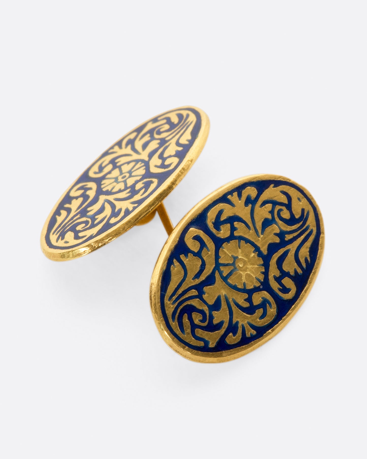 A pair of solid gold vintage cufflinks with intricate flourishes and contrasting dark blue enamel.